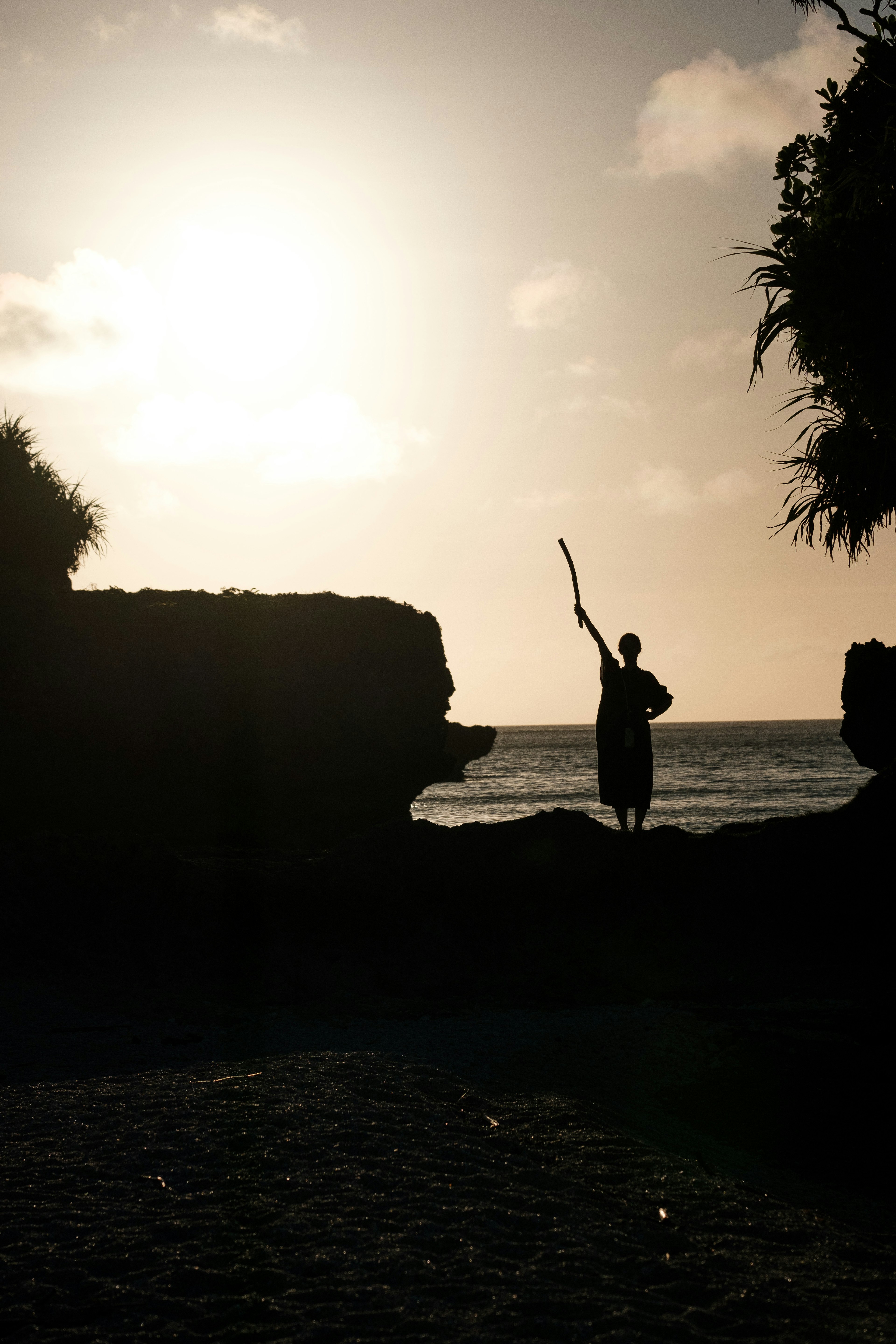 Silhouette di una persona con un bastone in piedi sulla spiaggia con il tramonto sullo sfondo