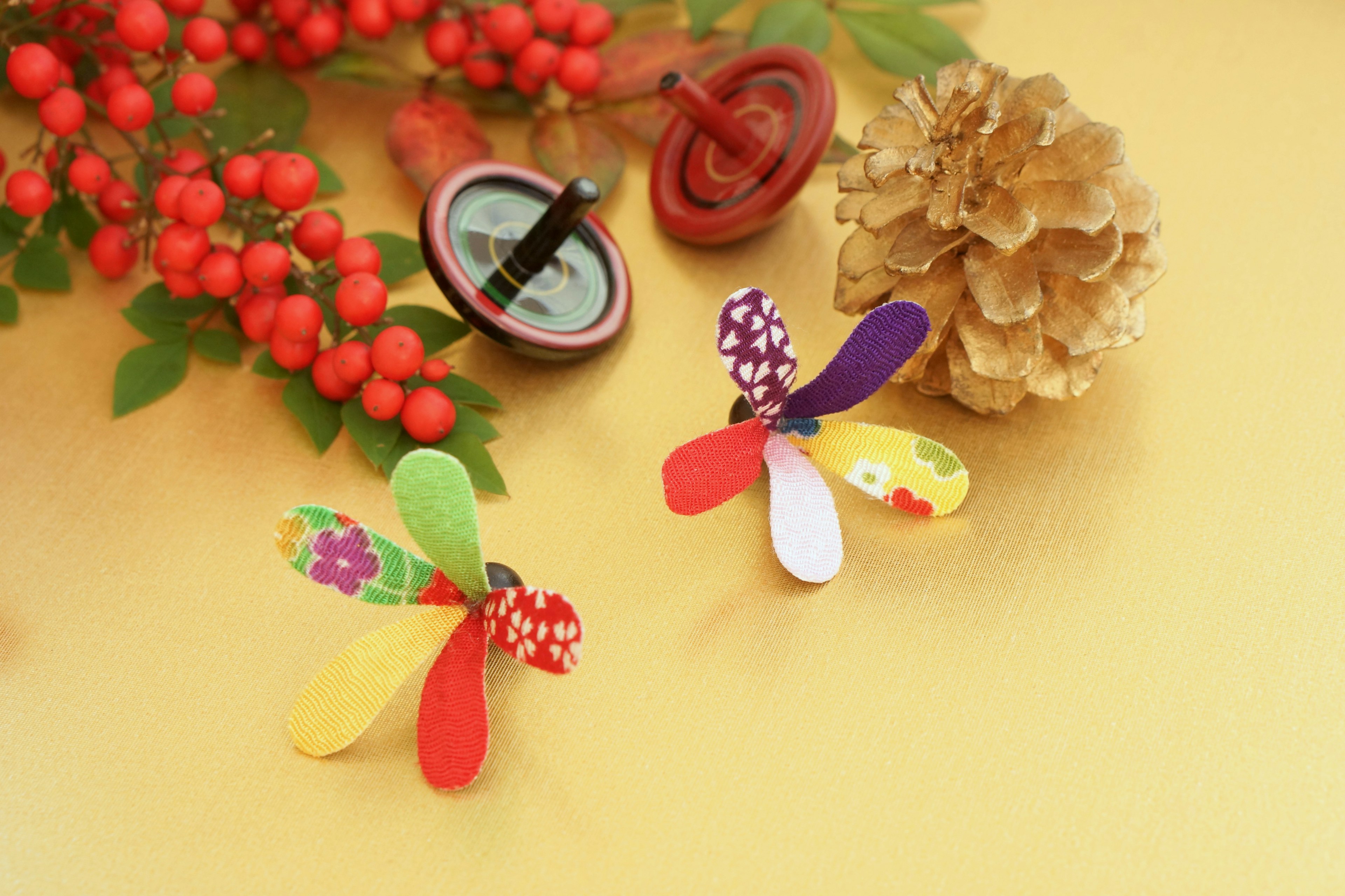 Dos decoraciones de papel colorido en forma de insectos junto a bayas rojas y una brújula sobre un fondo amarillo