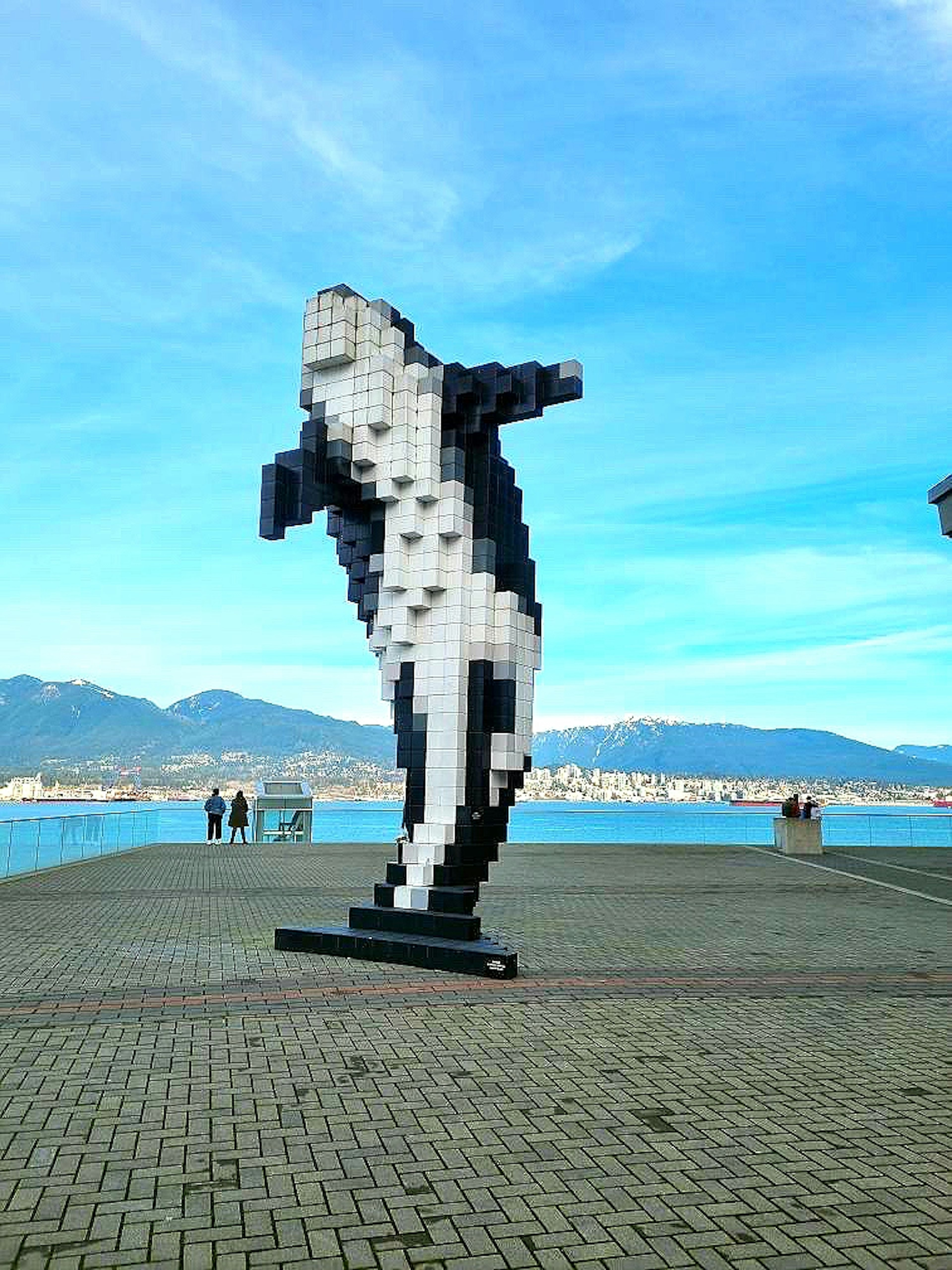 Große pixelierte Delphinskulptur in Schwarz und Weiß unter einem blauen Himmel