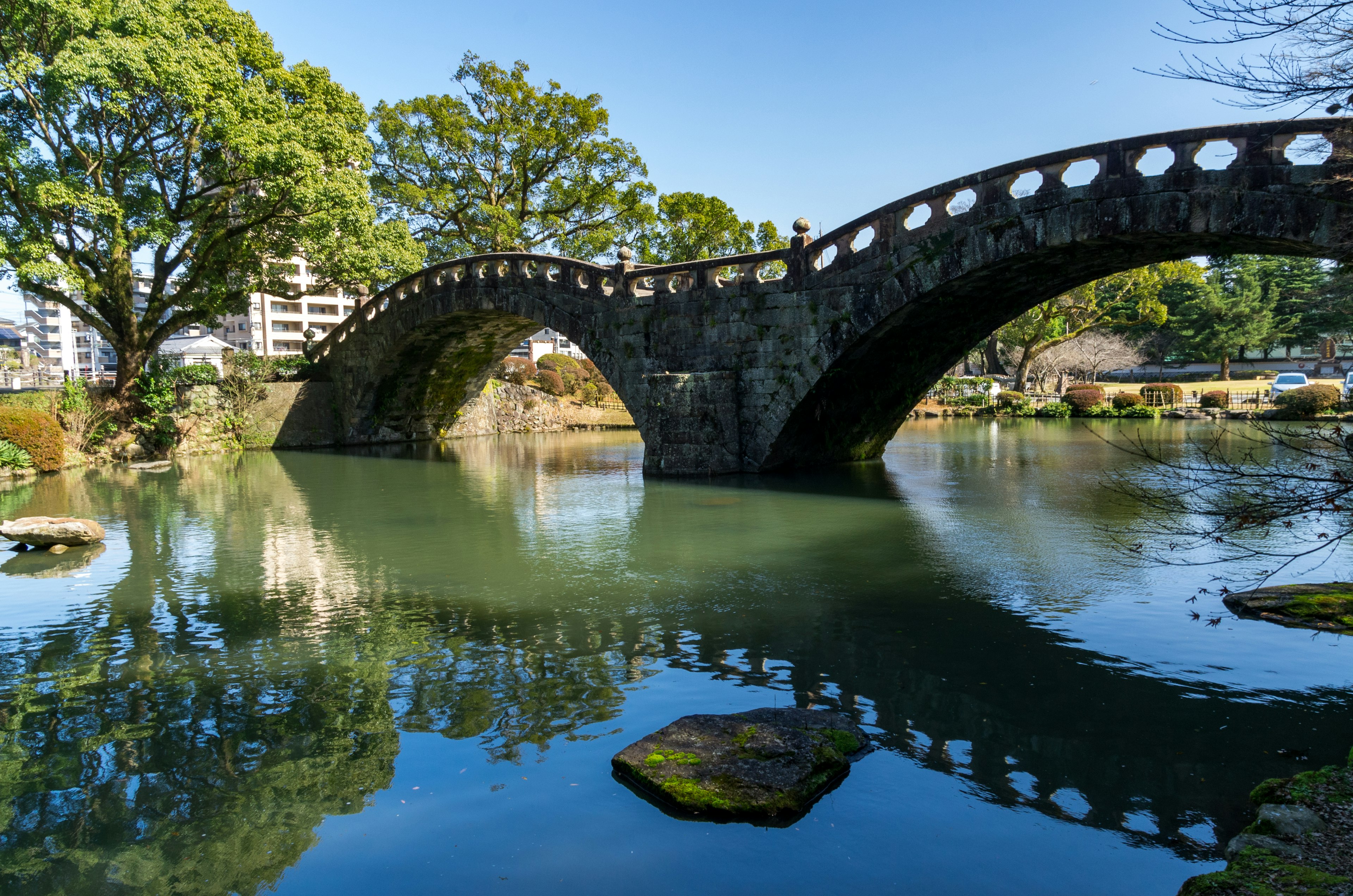 A beautiful stone bridge spans a tranquil pond surrounded by lush trees and reflections on the water