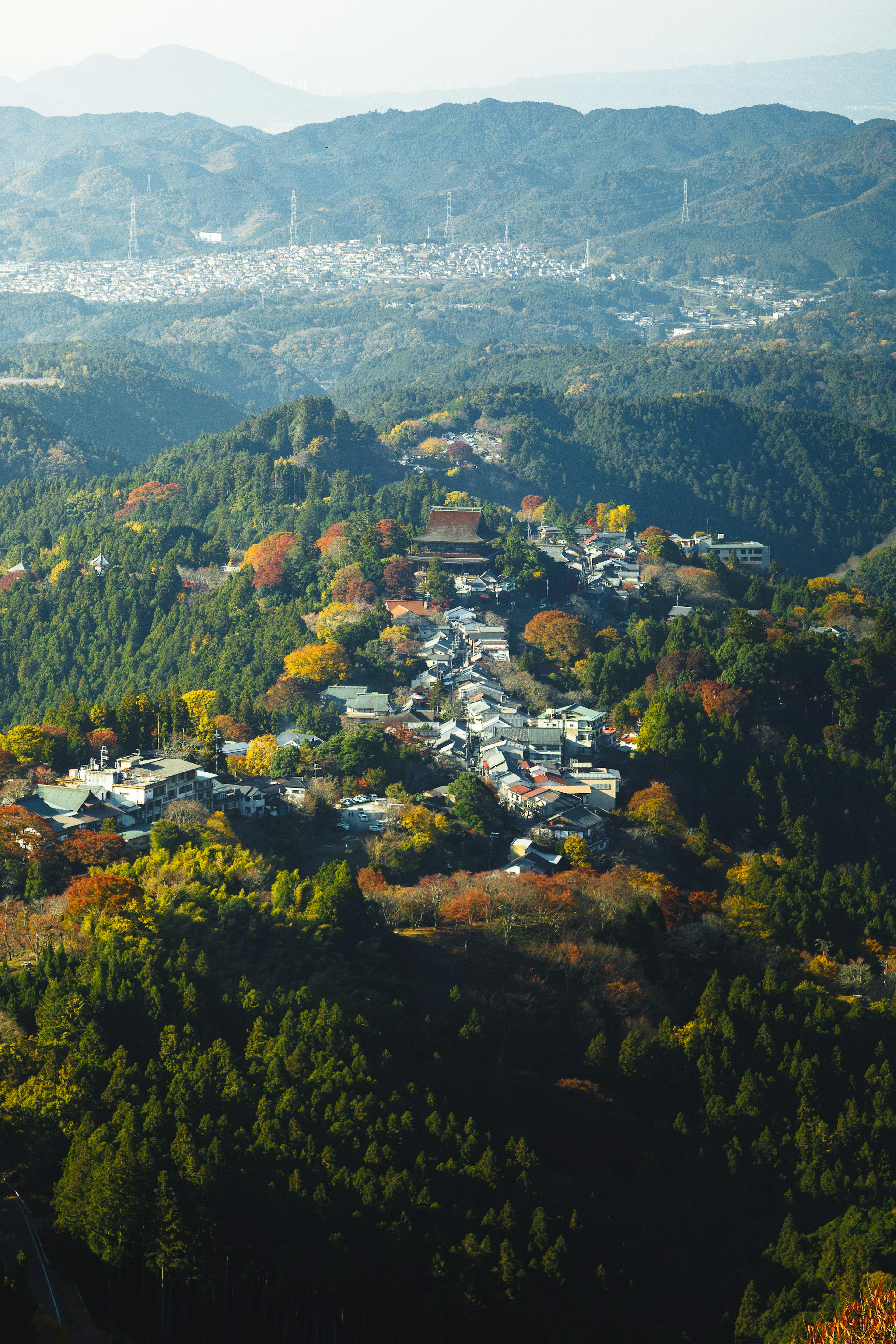 Ein Dorf umgeben von bunten Herbstbäumen, gesehen von einem Berggipfel