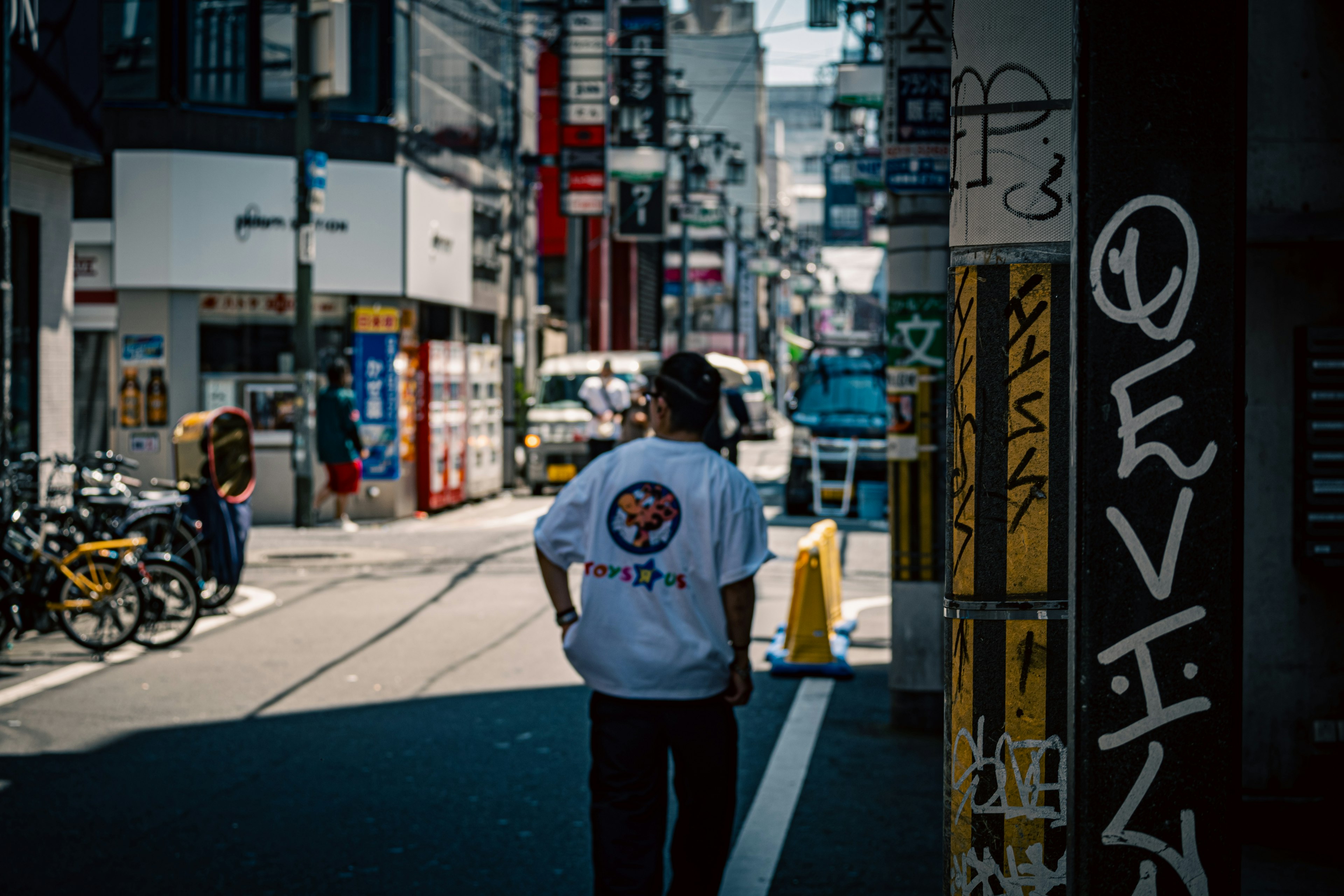 街中を歩く男性の後ろ姿 白いTシャツにはロゴがあり 自転車が並ぶ背景