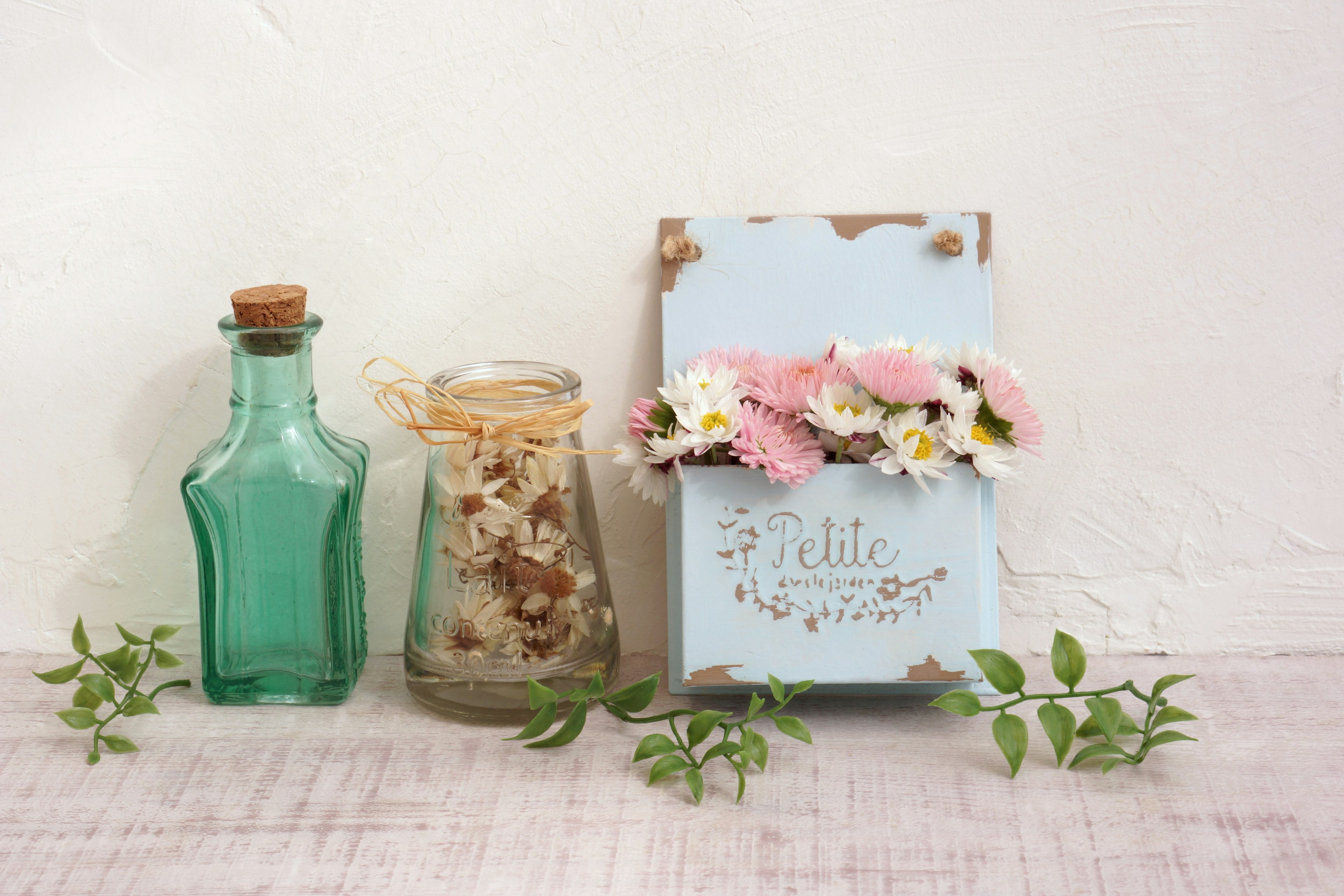 Scène décorative avec un panneau en bois bleu orné de fleurs et de bocaux en verre