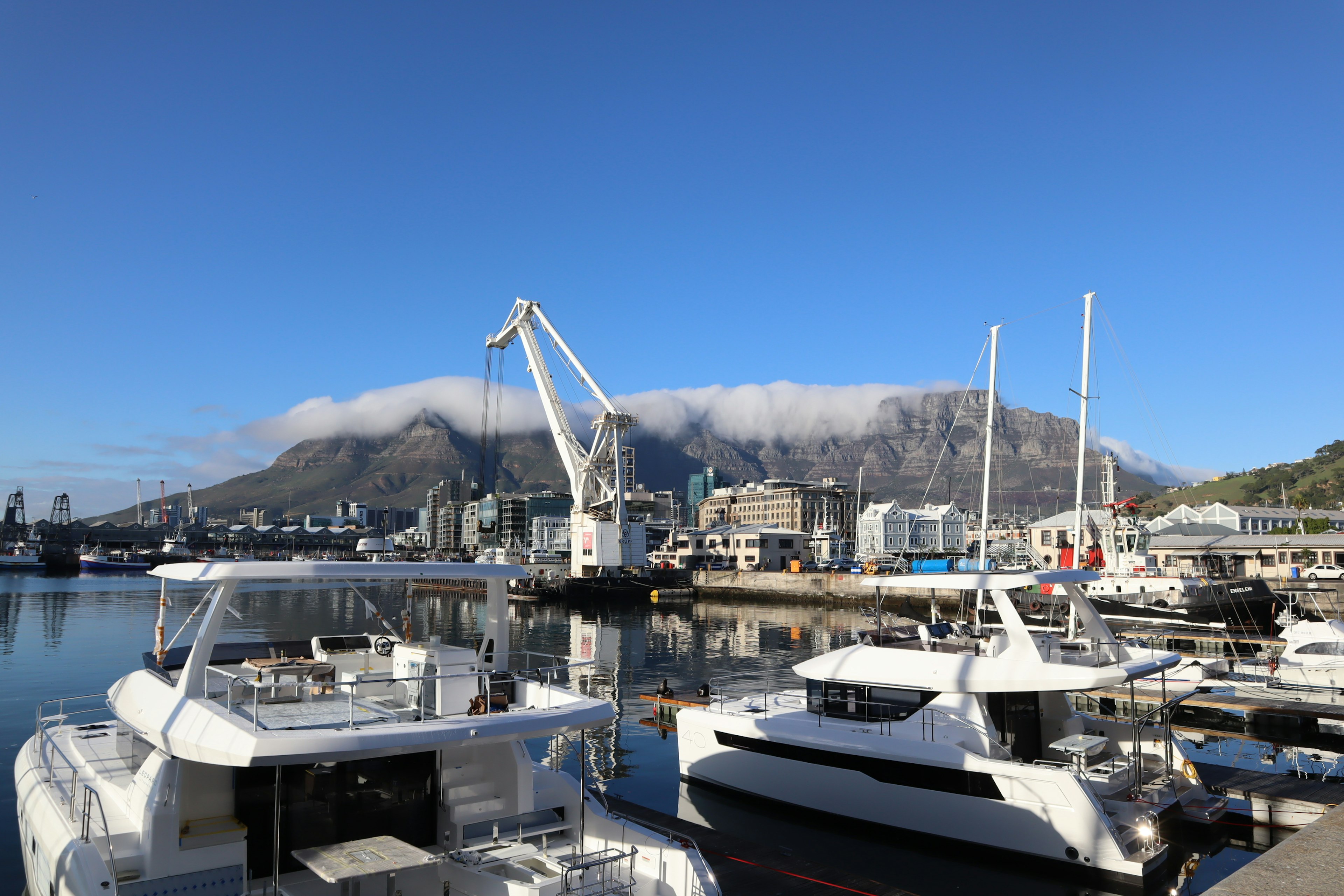 Scenic harbor view with white yachts and a crane, mountains covered in clouds in the background