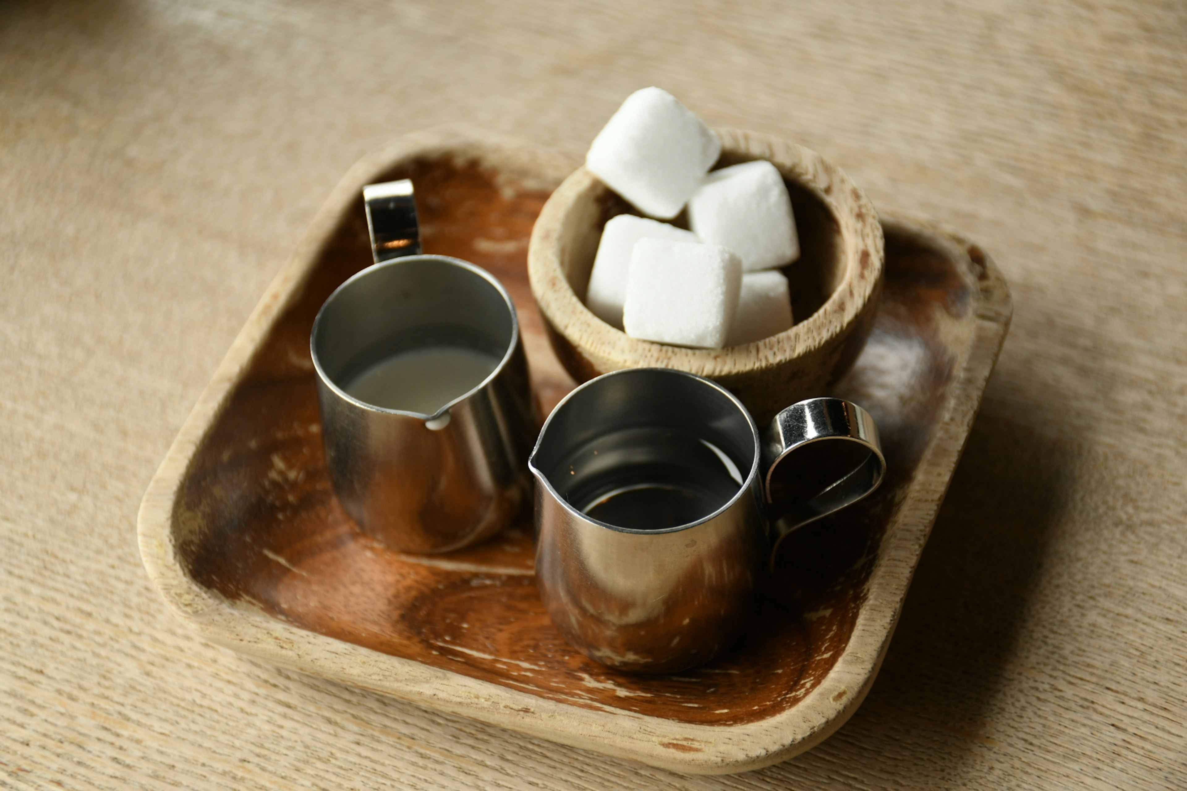 Ein Holztablett mit zwei Metallkännchen und einer Schüssel mit Zuckerwürfeln