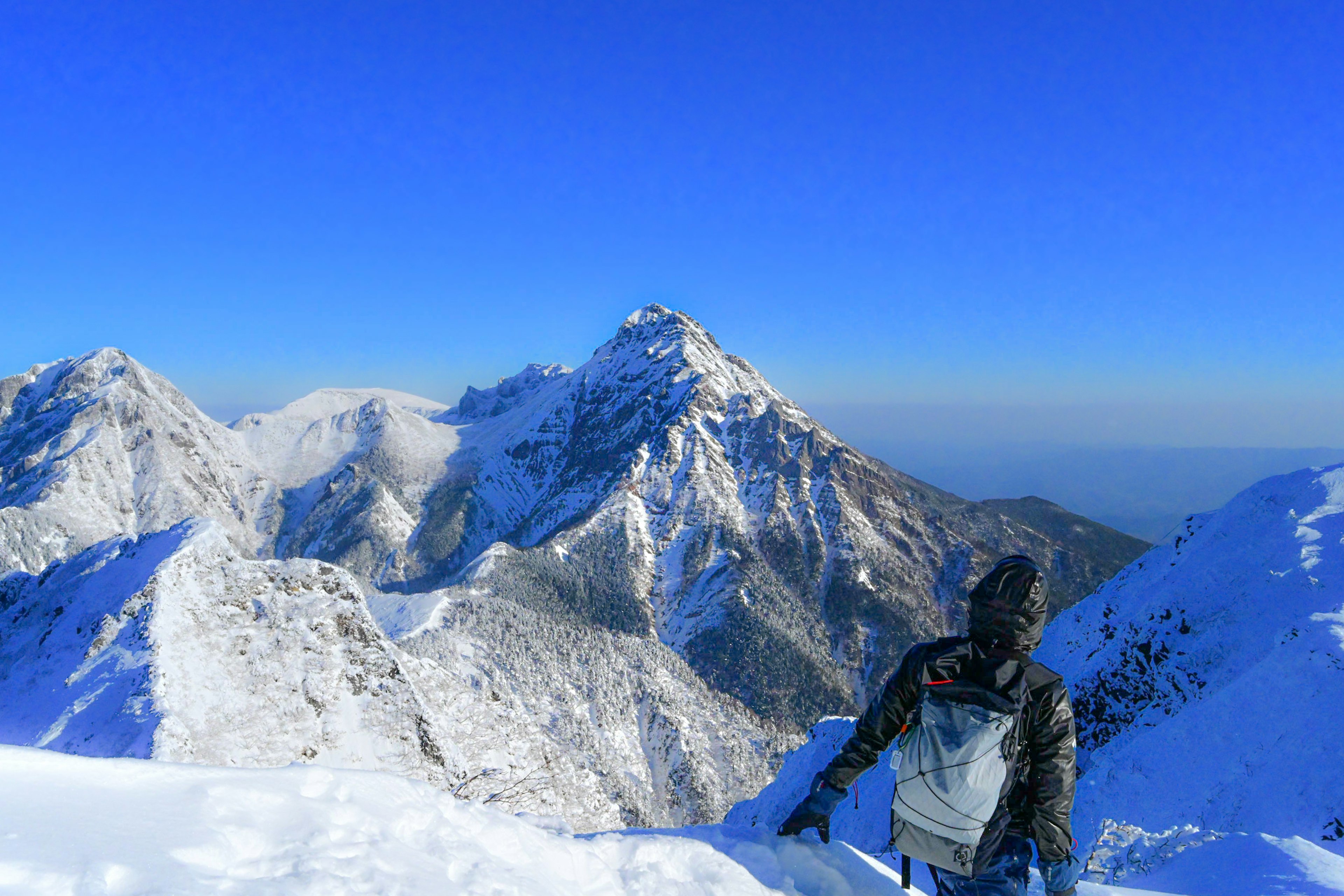 Hiker on snowy mountain peak with clear blue sky