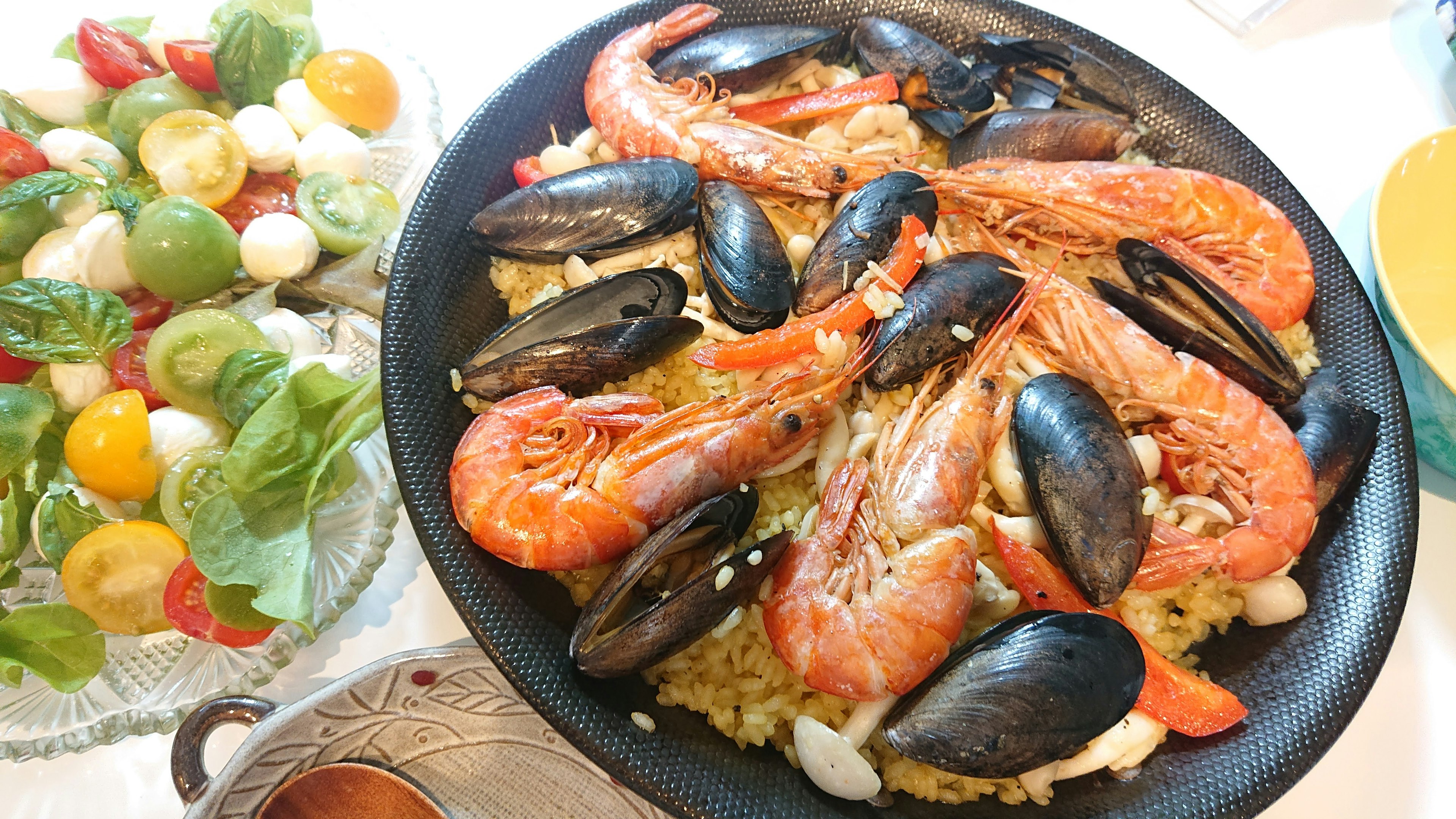 Paella seafood disajikan di piring hitam dengan salad samping