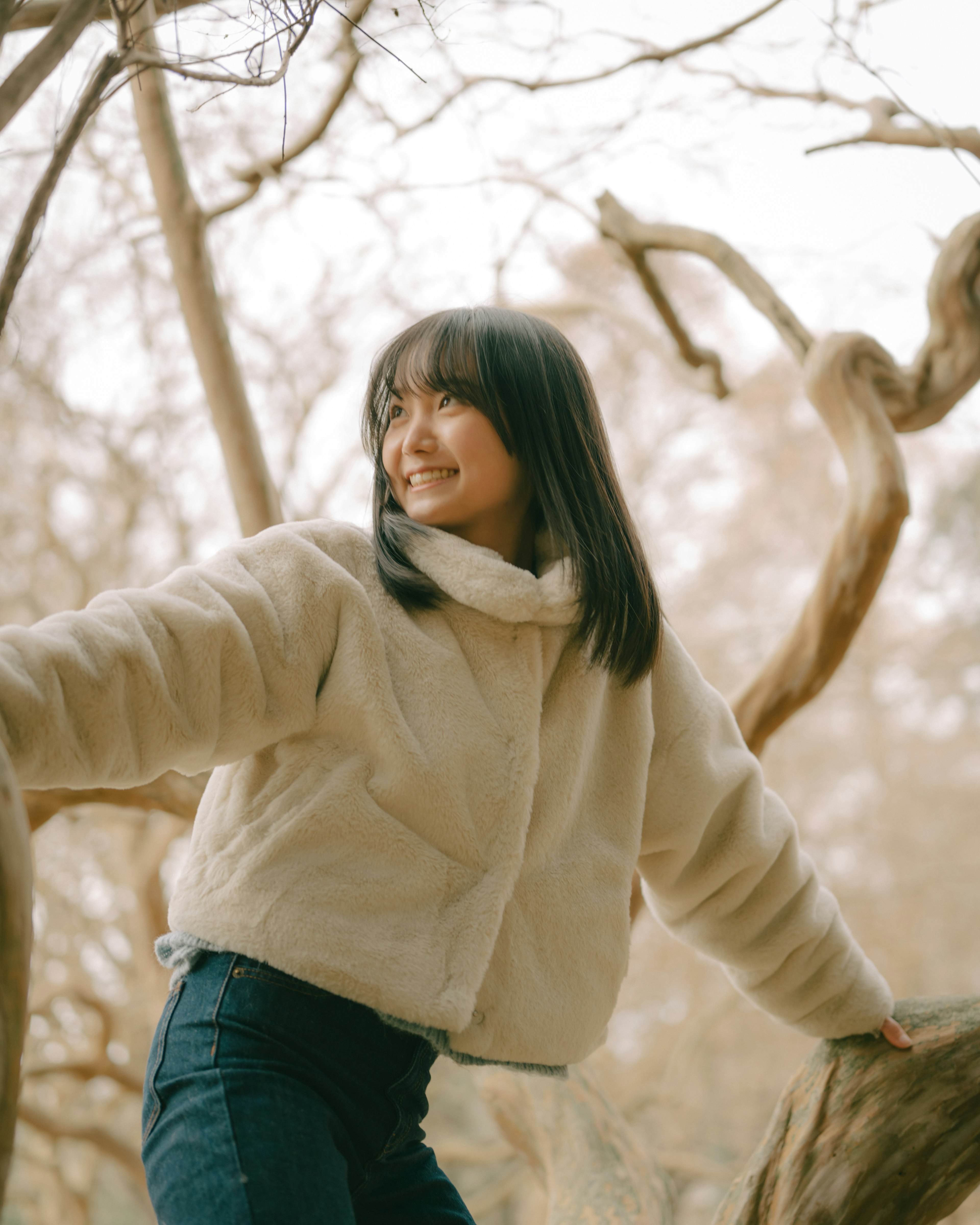 Smiling woman leaning on a tree branch wearing winter clothing in a natural setting