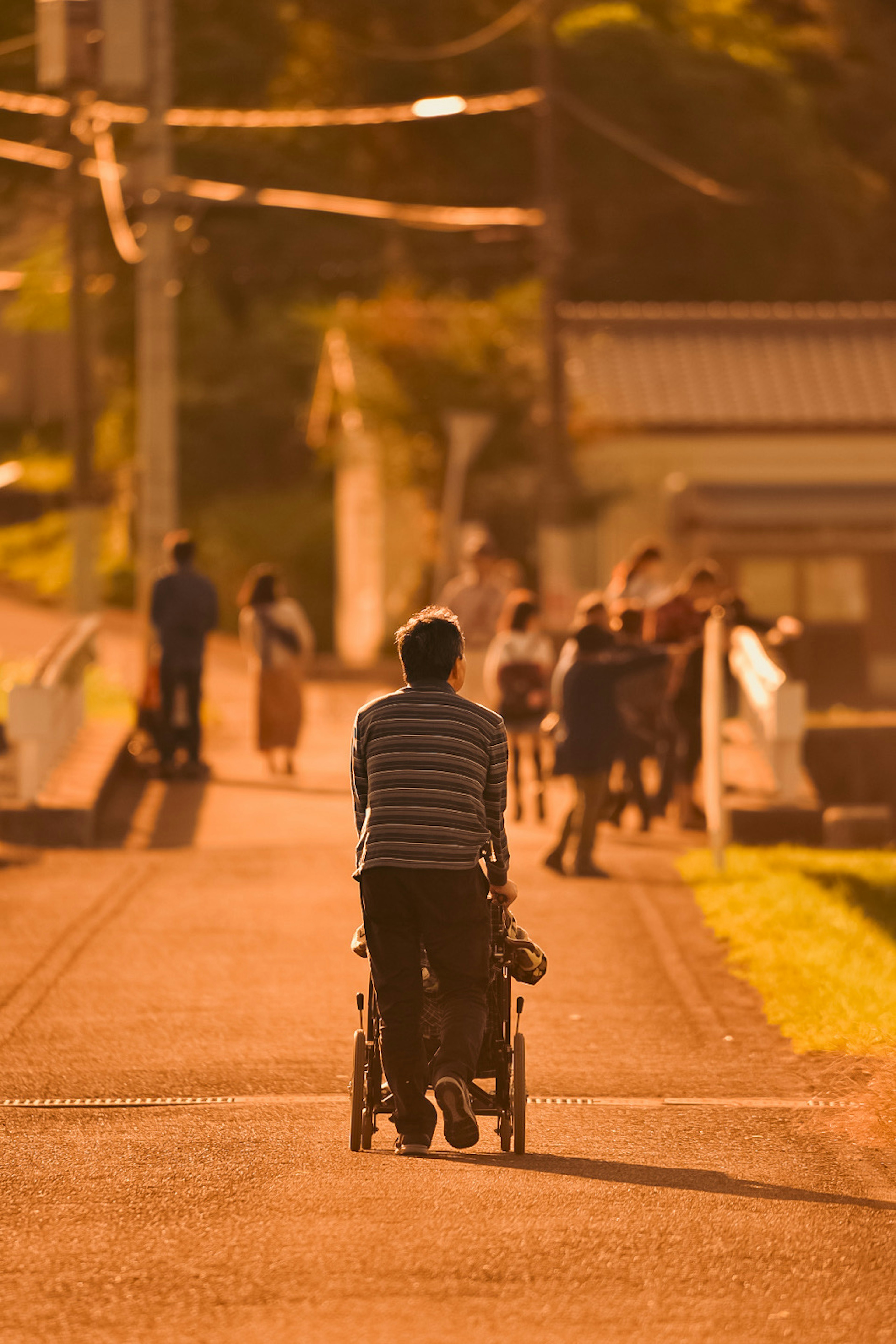 Un uomo che spinge un passeggino camminando lungo una strada con luce di tramonto