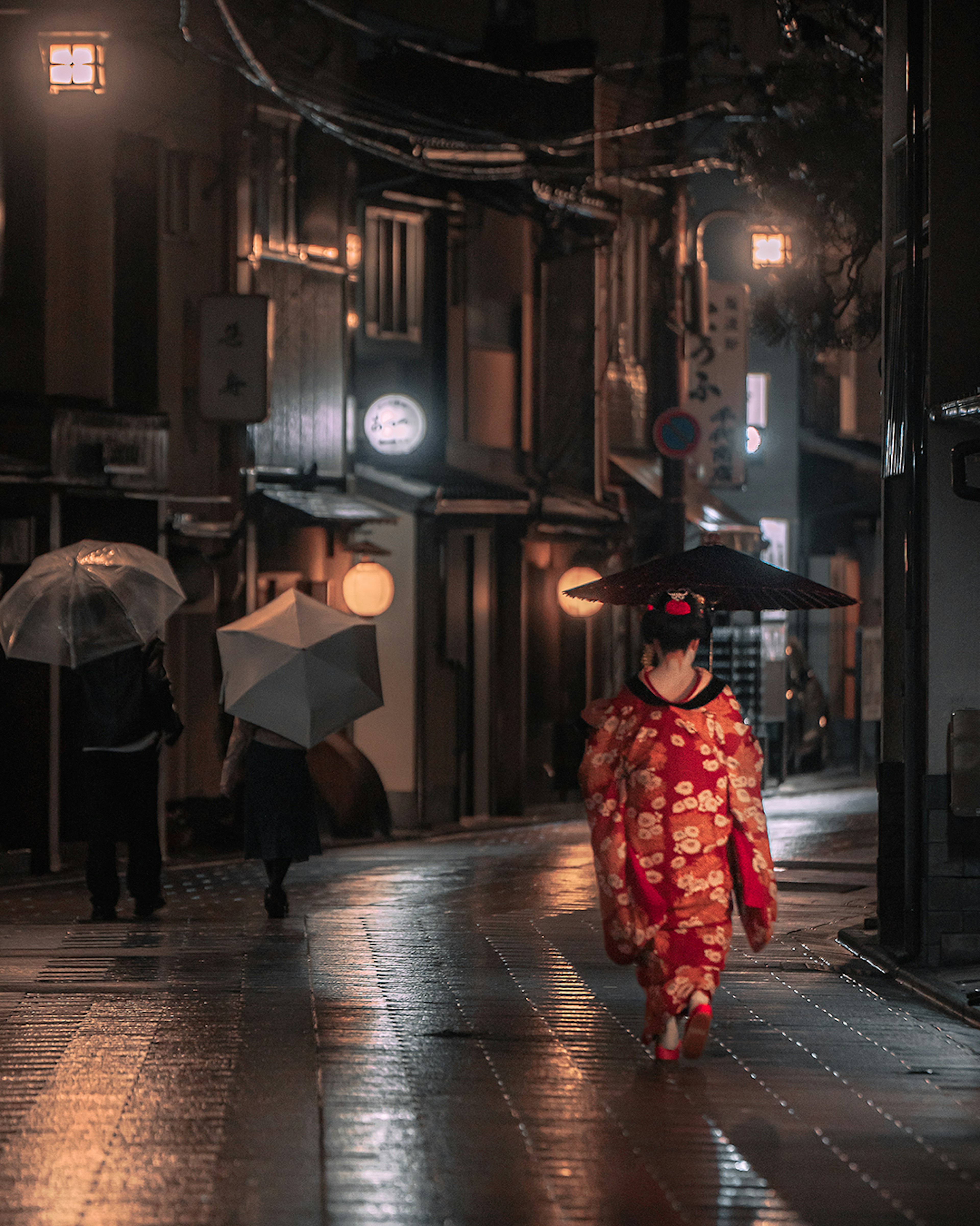 Une femme en kimono marchant dans une rue pluvieuse avec des parapluies en arrière-plan