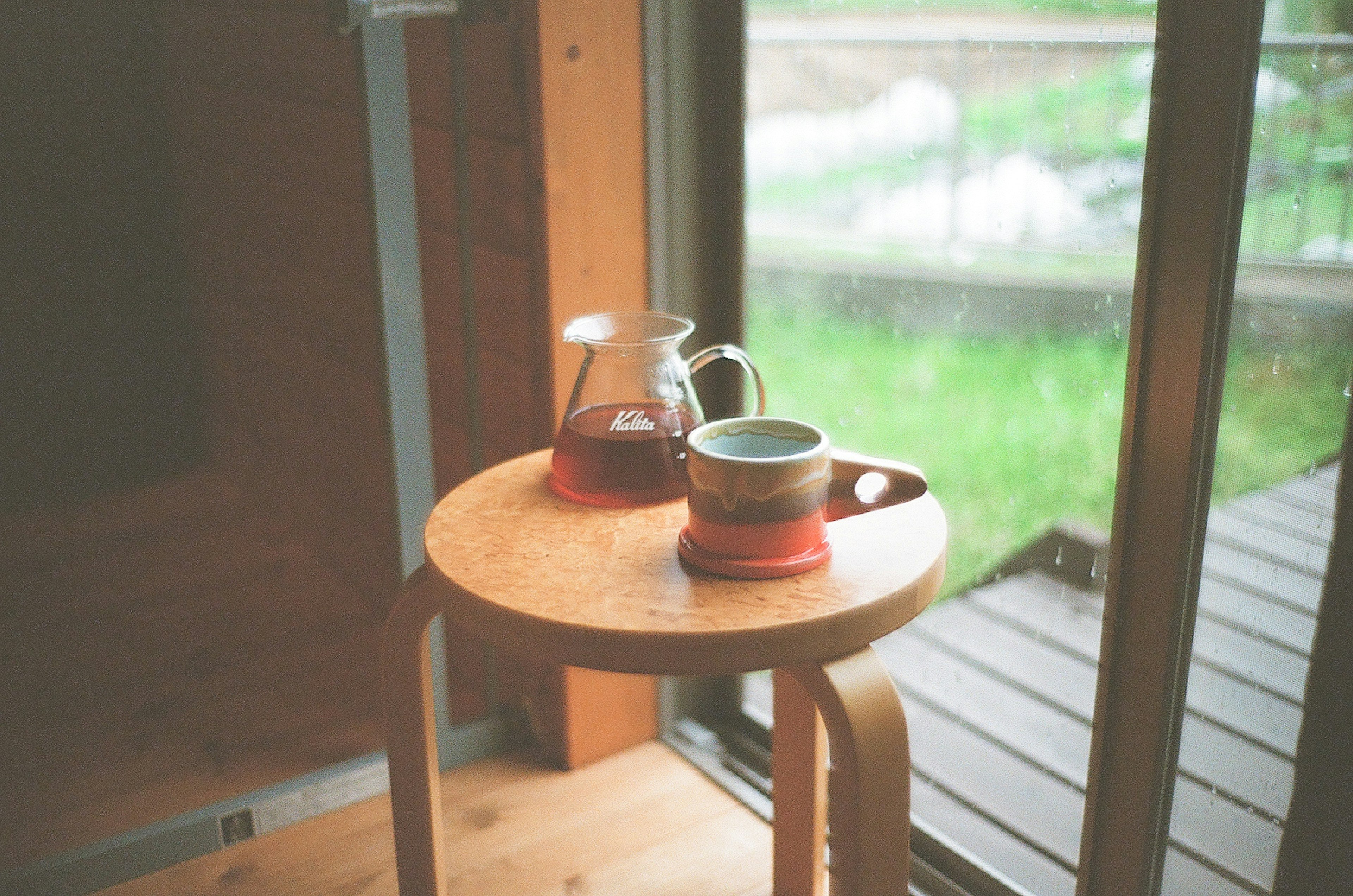 Una mesa de madera junto a la ventana con una tetera y una taza