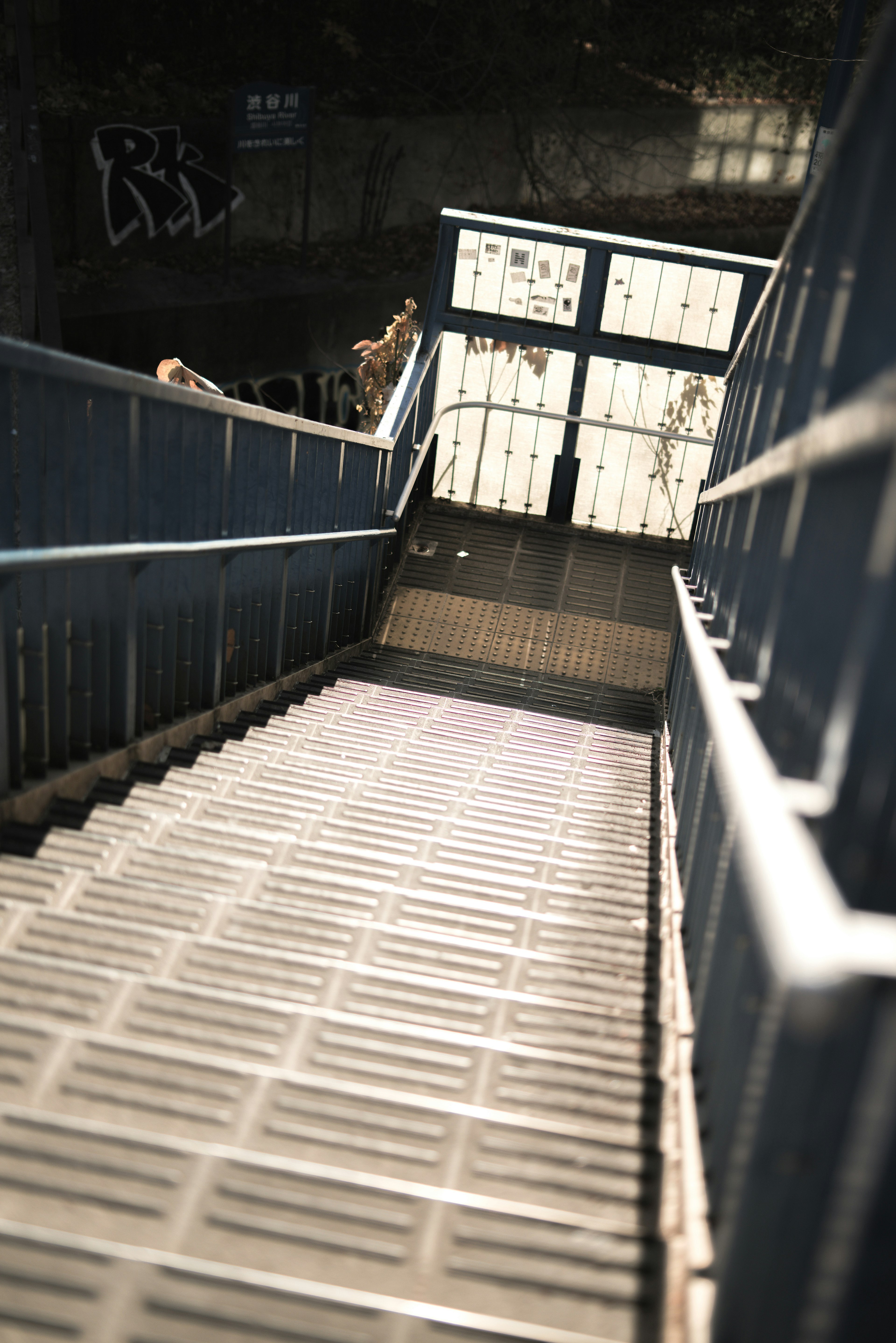 Scala che scende verso un'entrata della metropolitana con corrimano blu