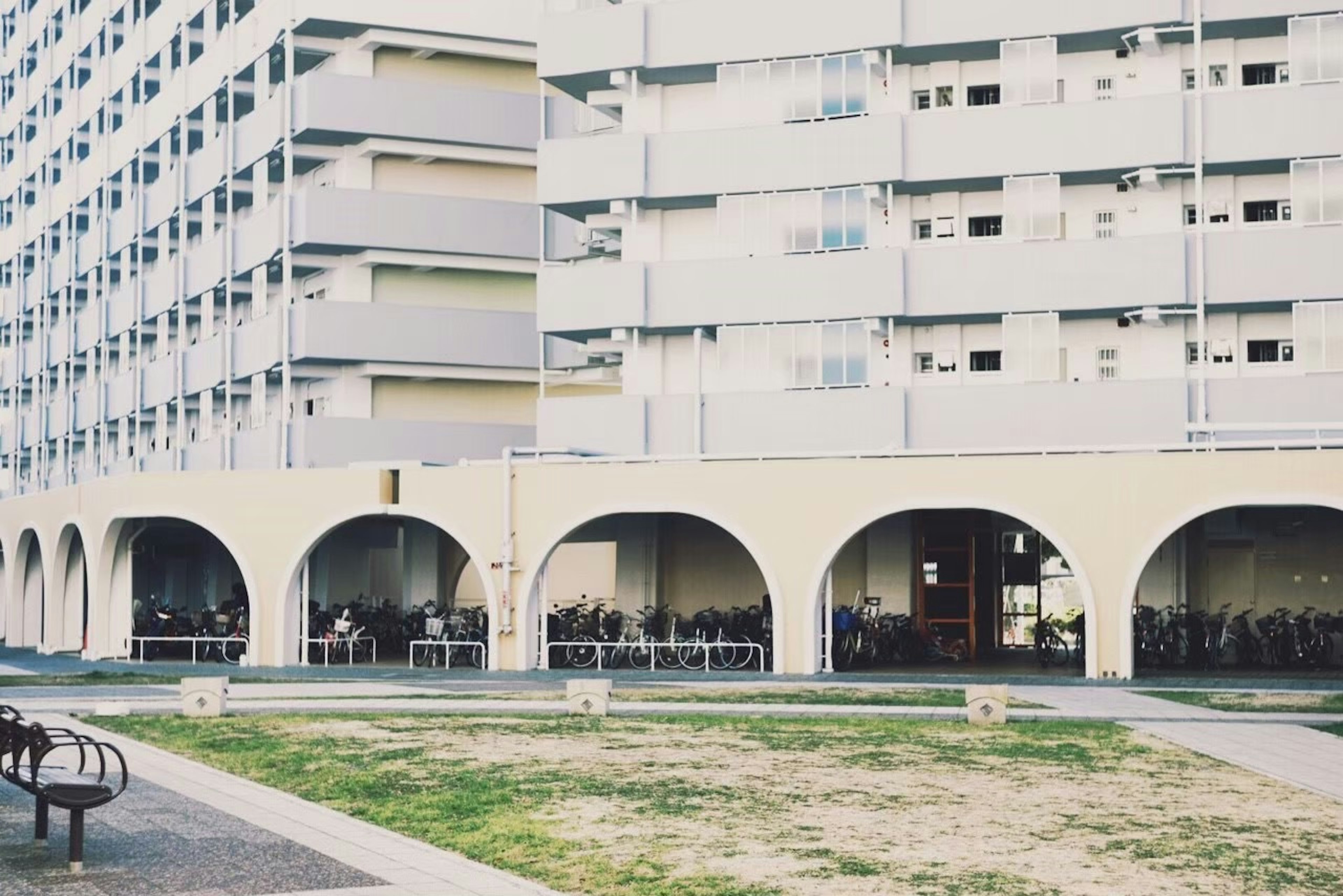 Parte de un edificio de apartamentos con estructuras de arco blanco y un área de césped