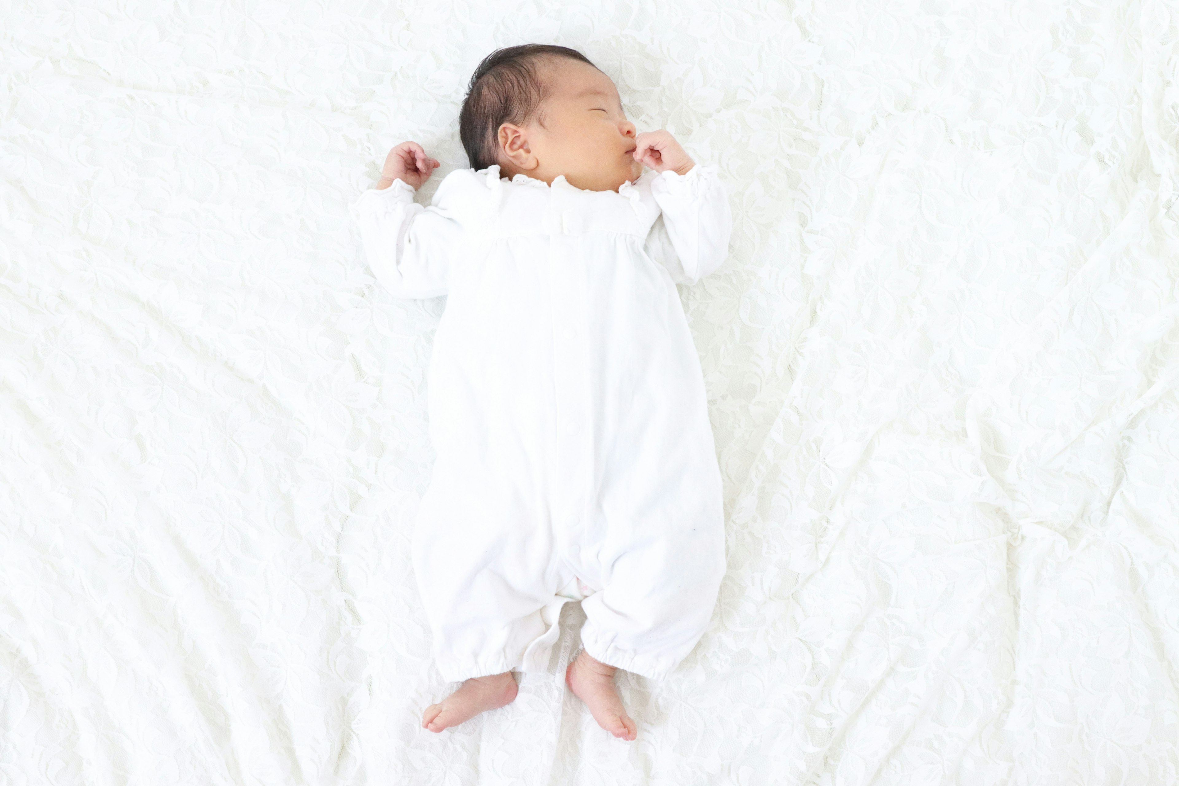 Baby sleeping on a white blanket wearing a white outfit