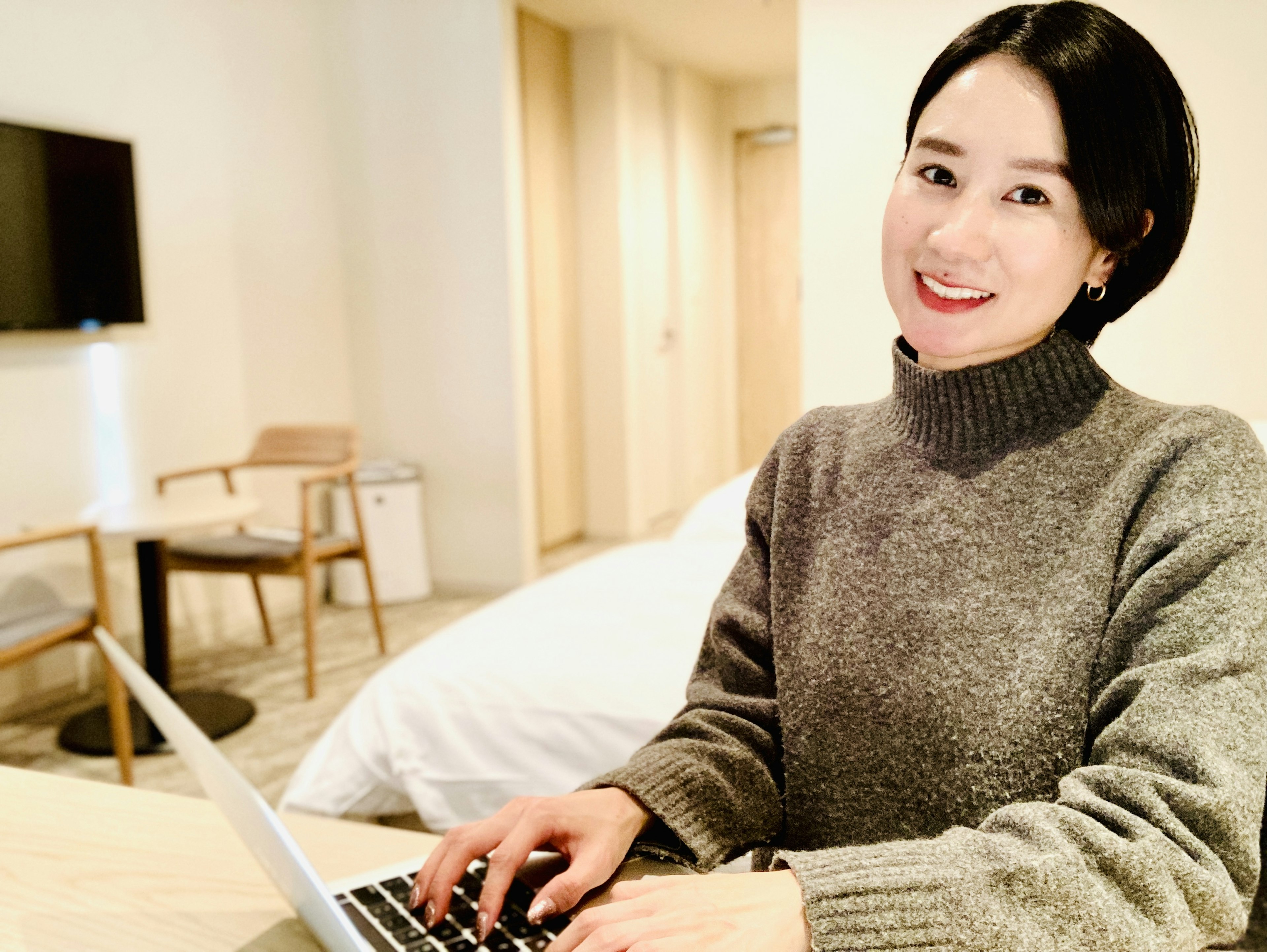 Woman in gray sweater working on laptop in hotel room