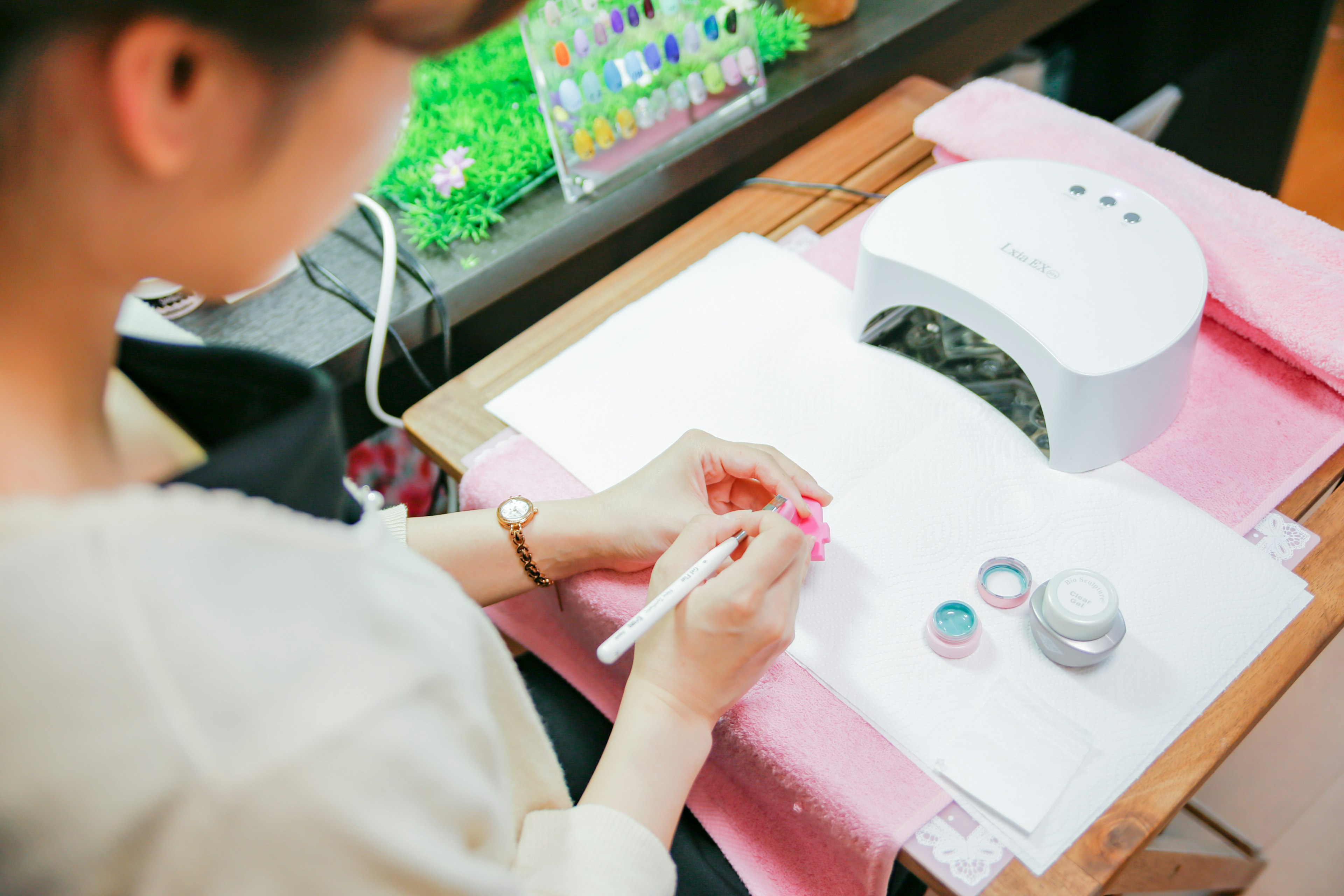 Mujer aplicando arte de uñas con lámpara UV y polvos coloridos