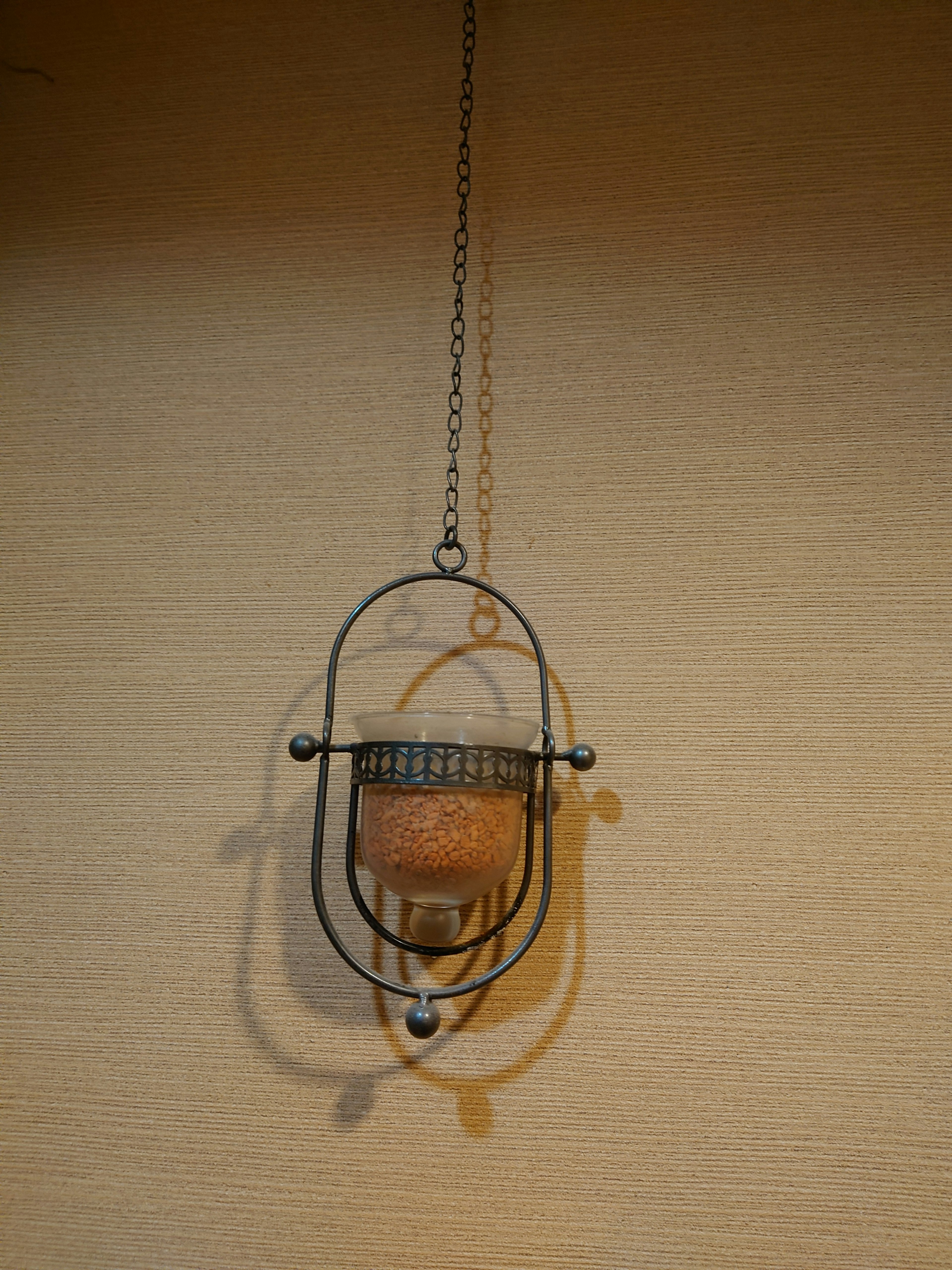 A metal hanging lantern with a glass container is suspended from the wall