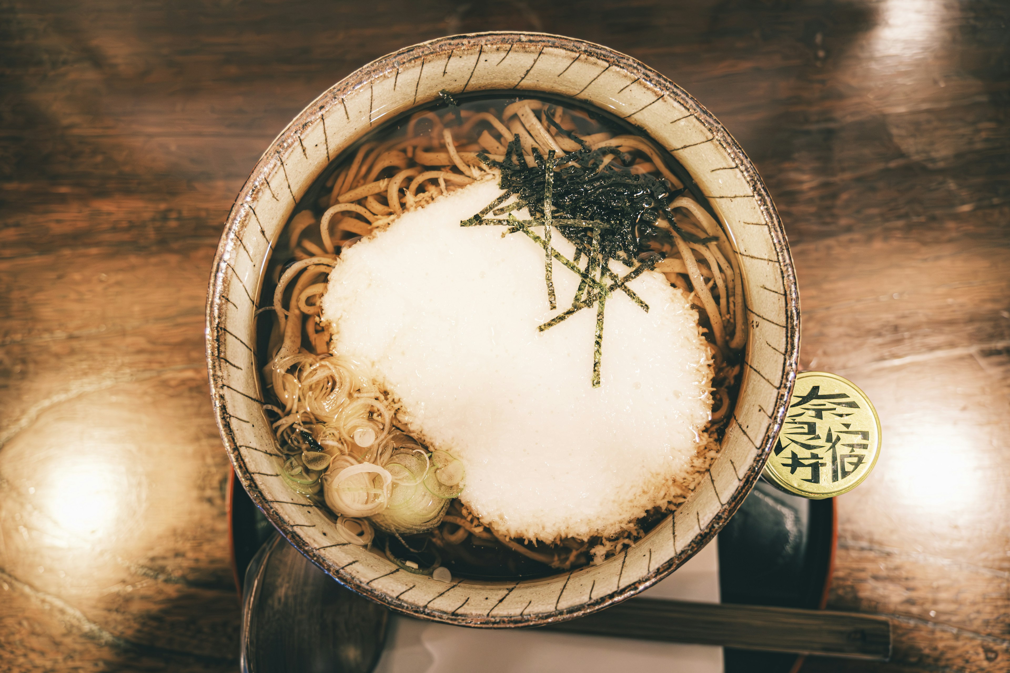 A bowl of soba noodles topped with a dollop of white substance and garnished with seaweed