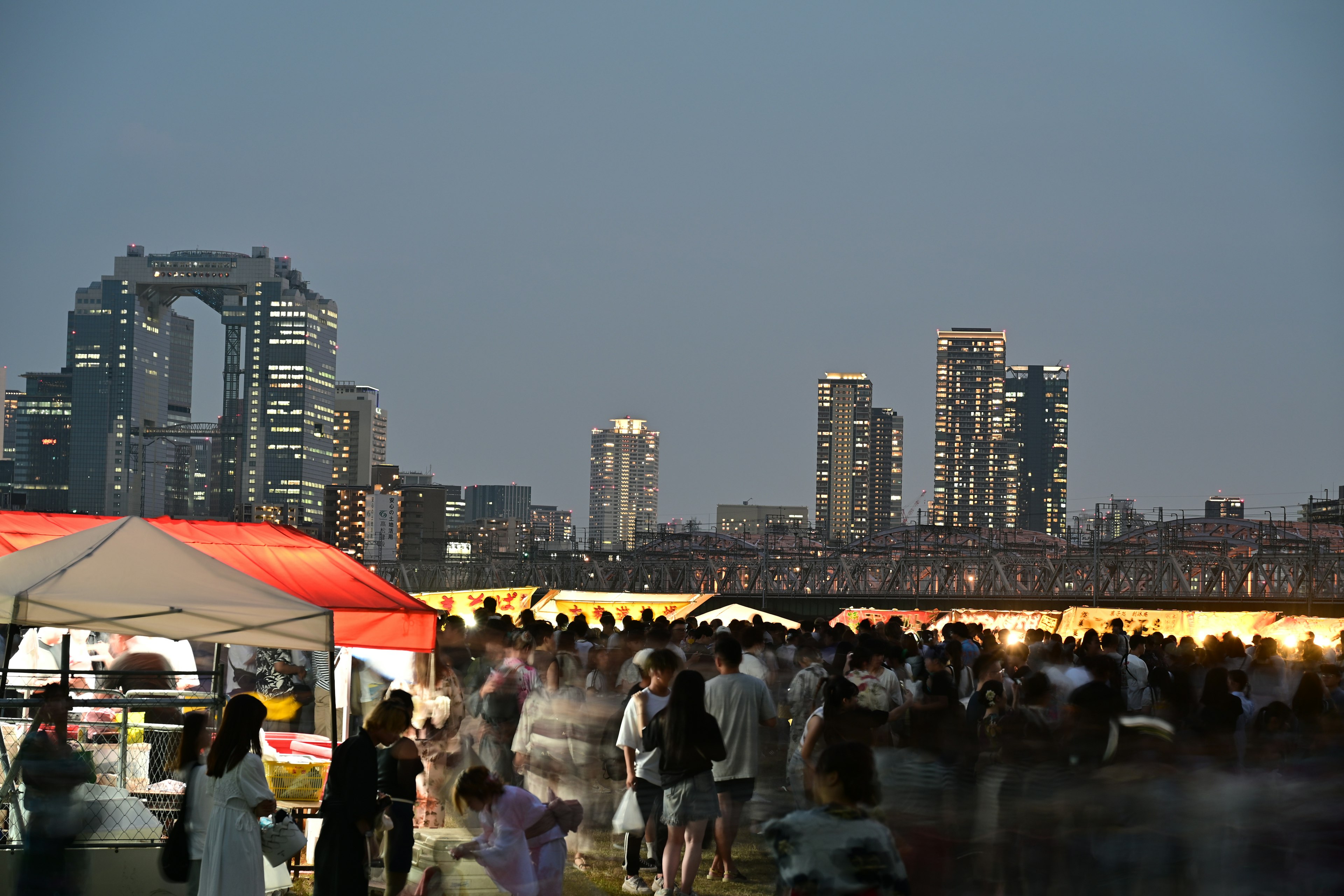 Crowd gathering at a rooftop during twilight with food stalls and city skyline