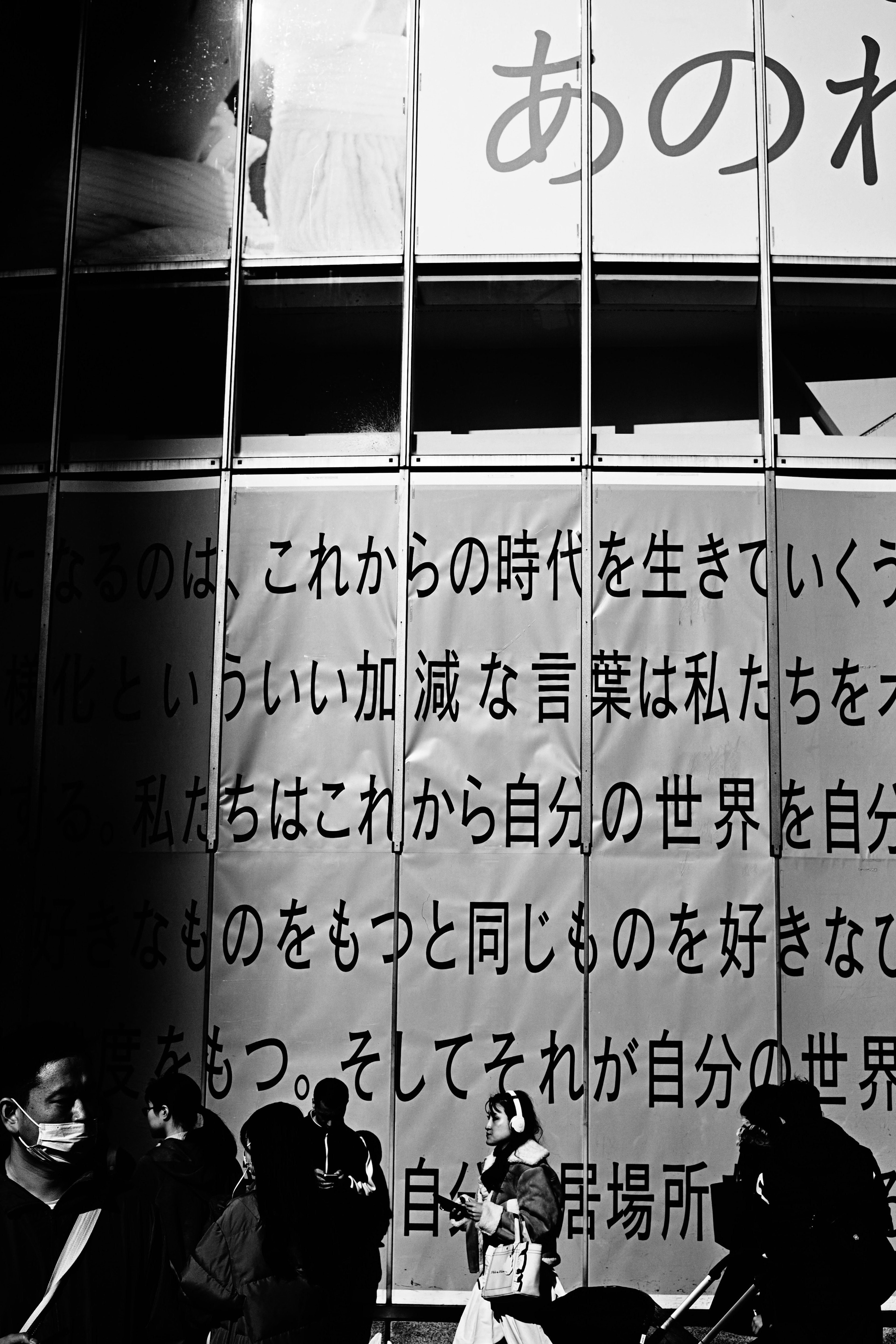 Black and white photo of people walking by a wall with large text