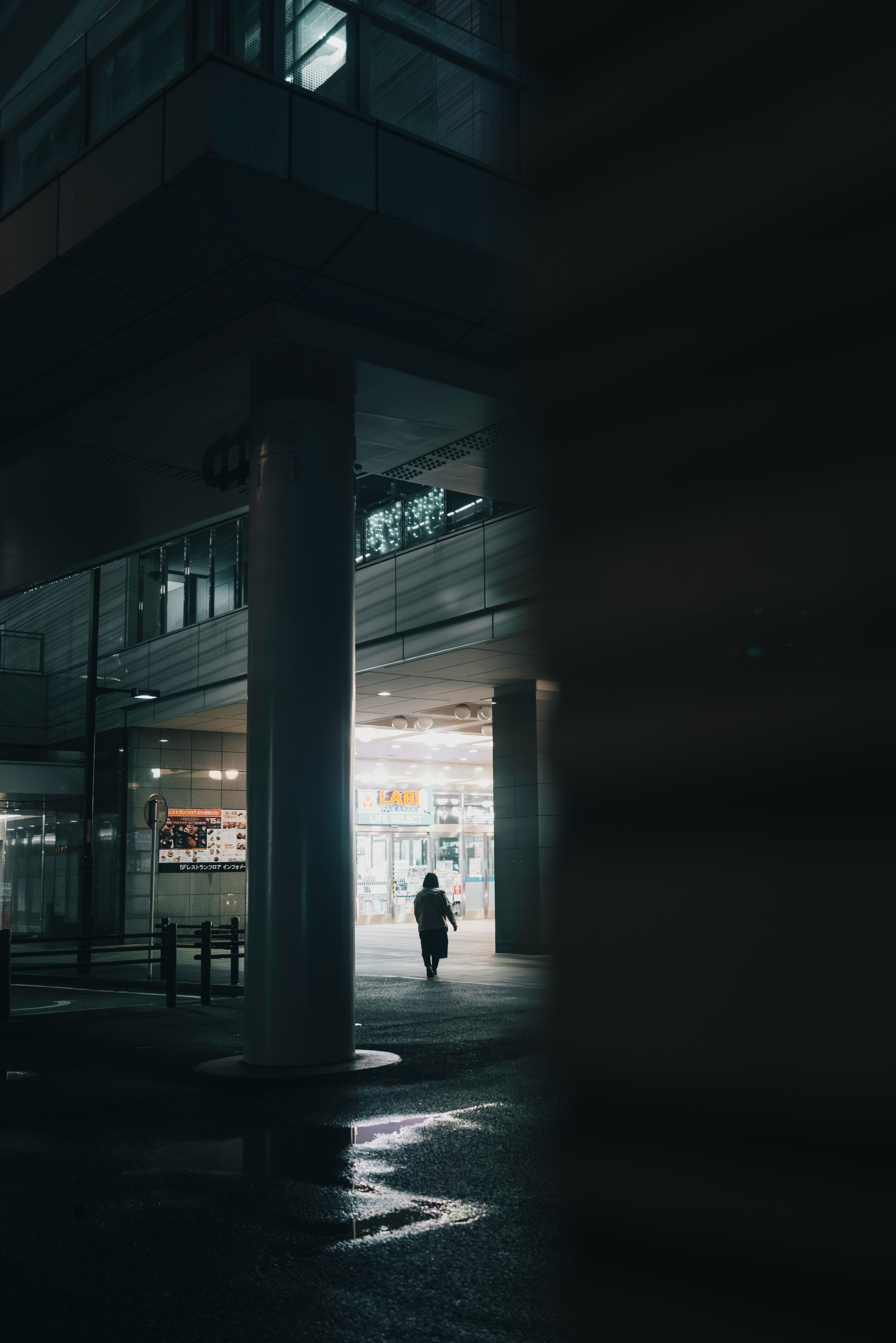 Silhouette of a person walking under a dim building with bright entrance light