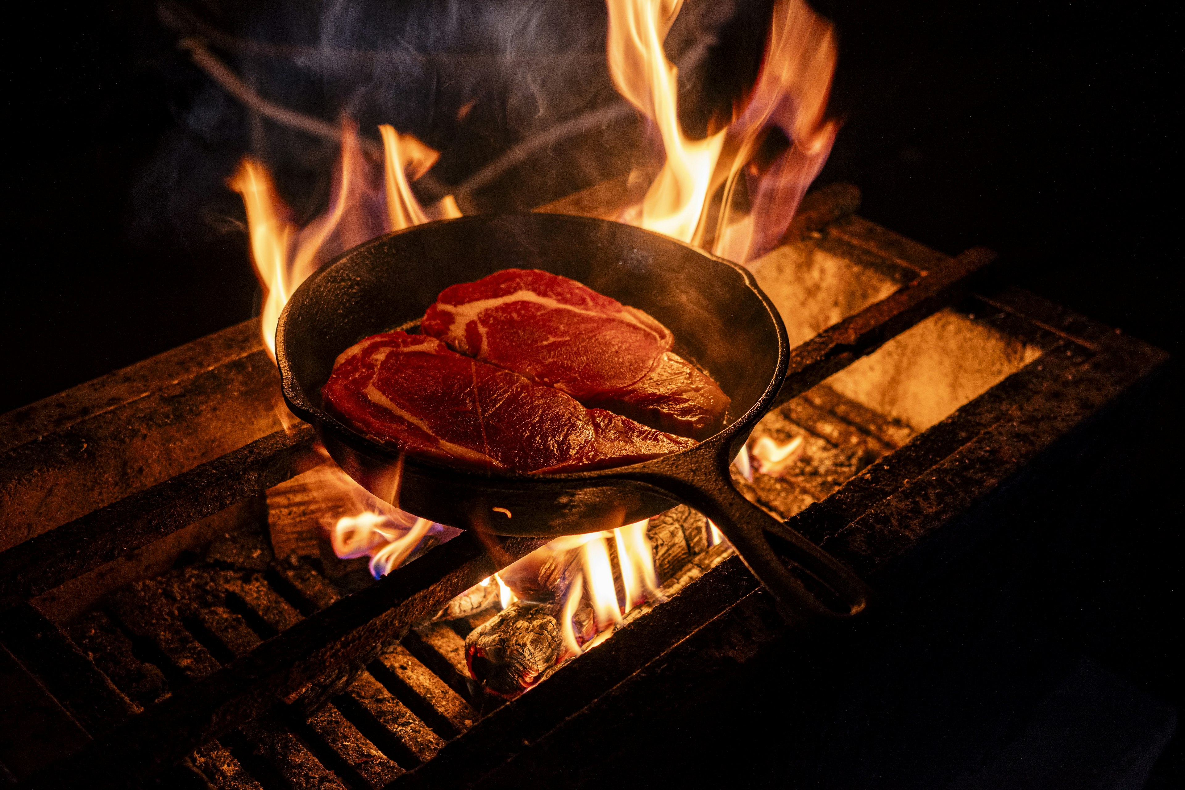 Un morceau de viande grésillant dans une poêle en fonte sur une flamme ouverte