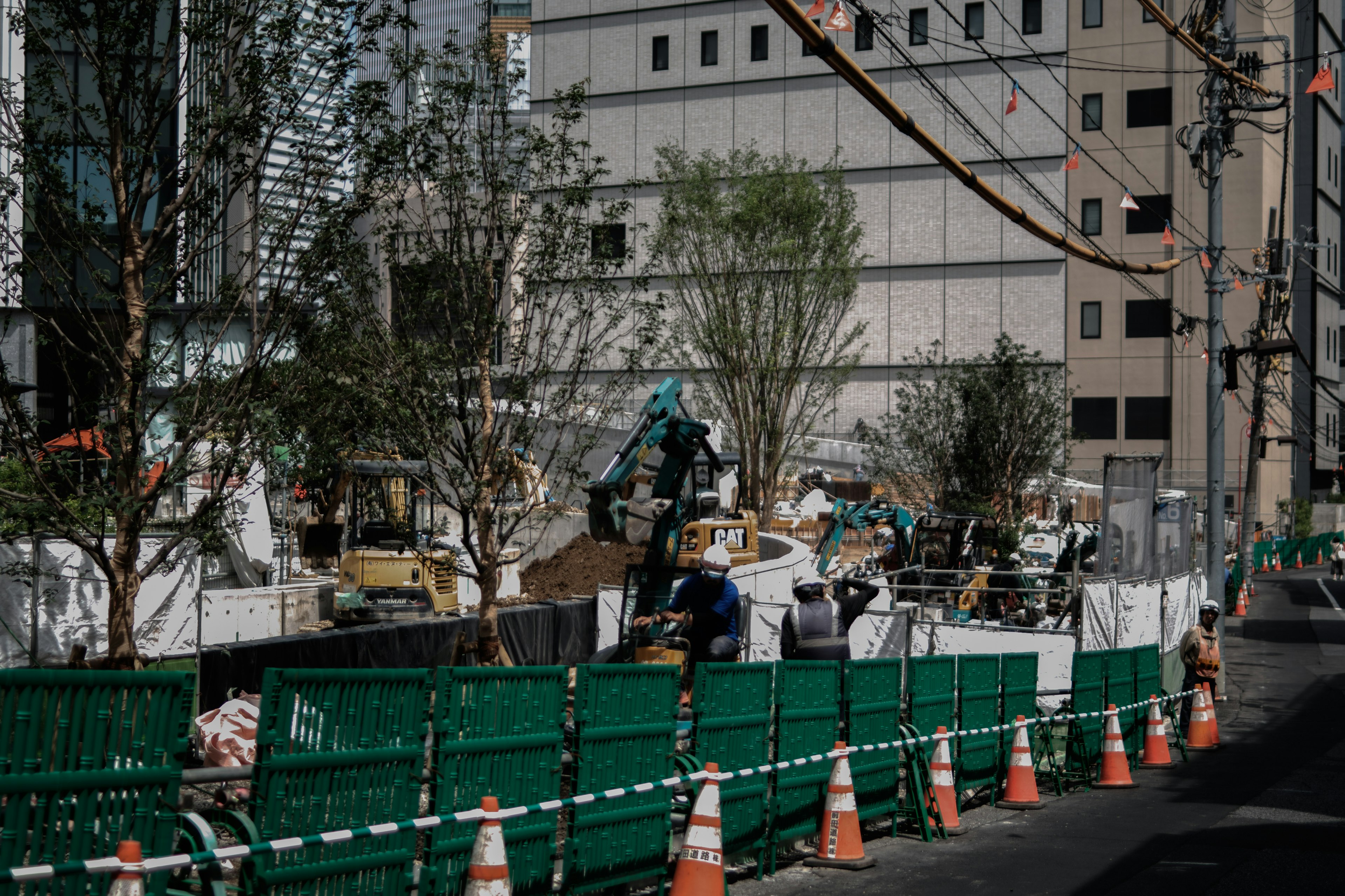 Sitio de construcción urbano con cercado verde y maquinaria pesada