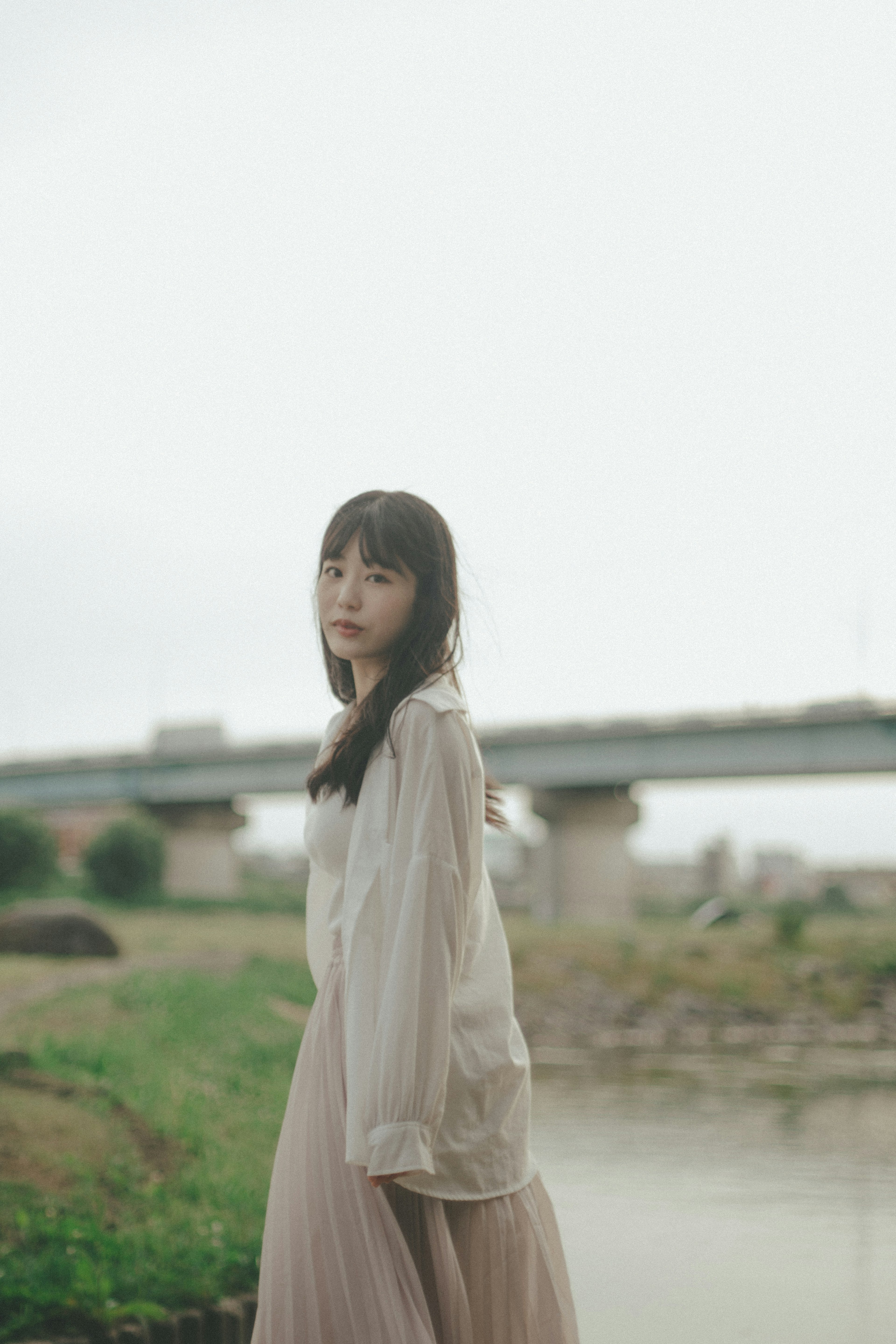 A woman standing by the riverside with a soft dress and a serene expression