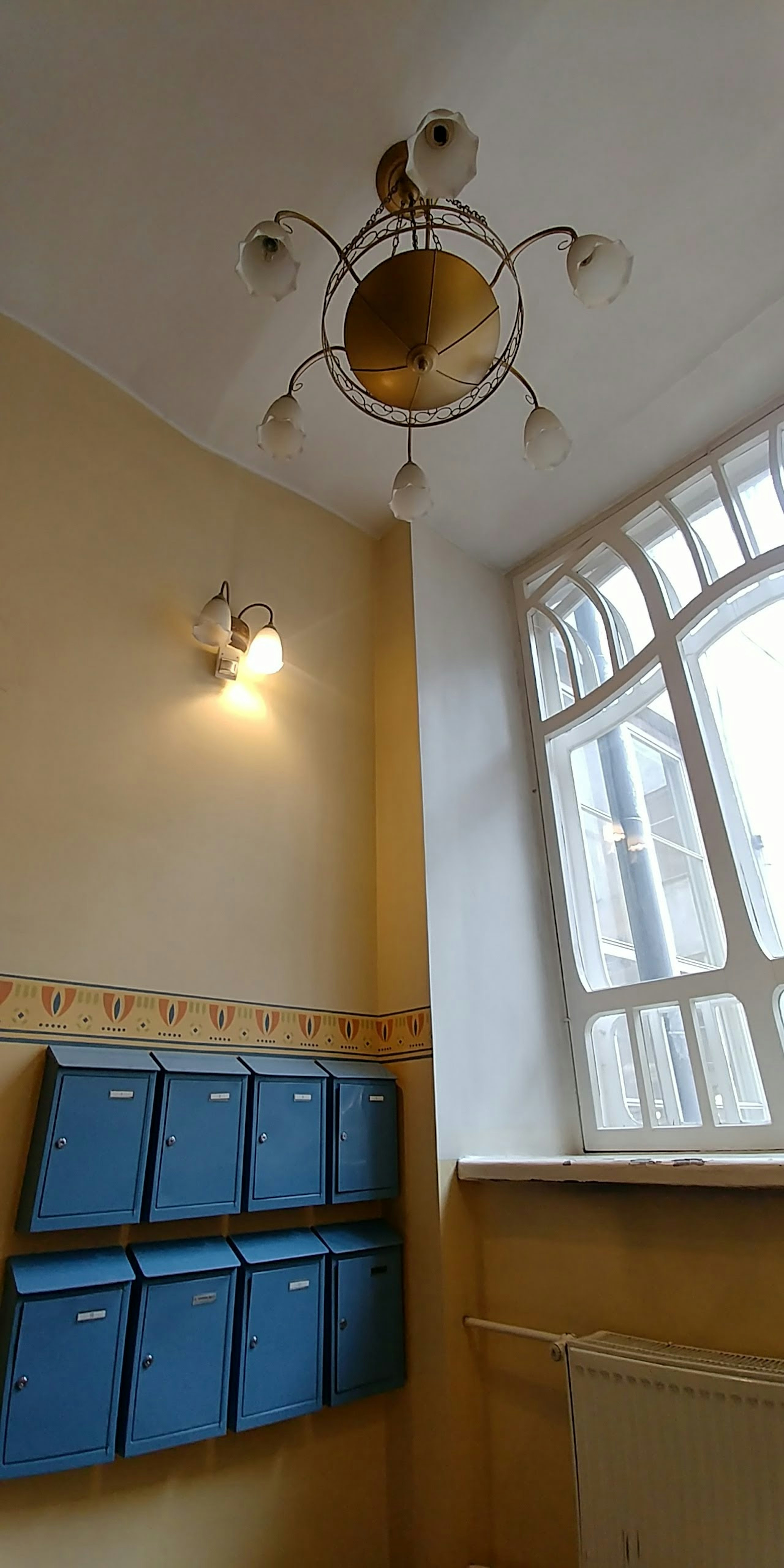 Interior corner with blue mailboxes against light-colored walls and a decorative chandelier