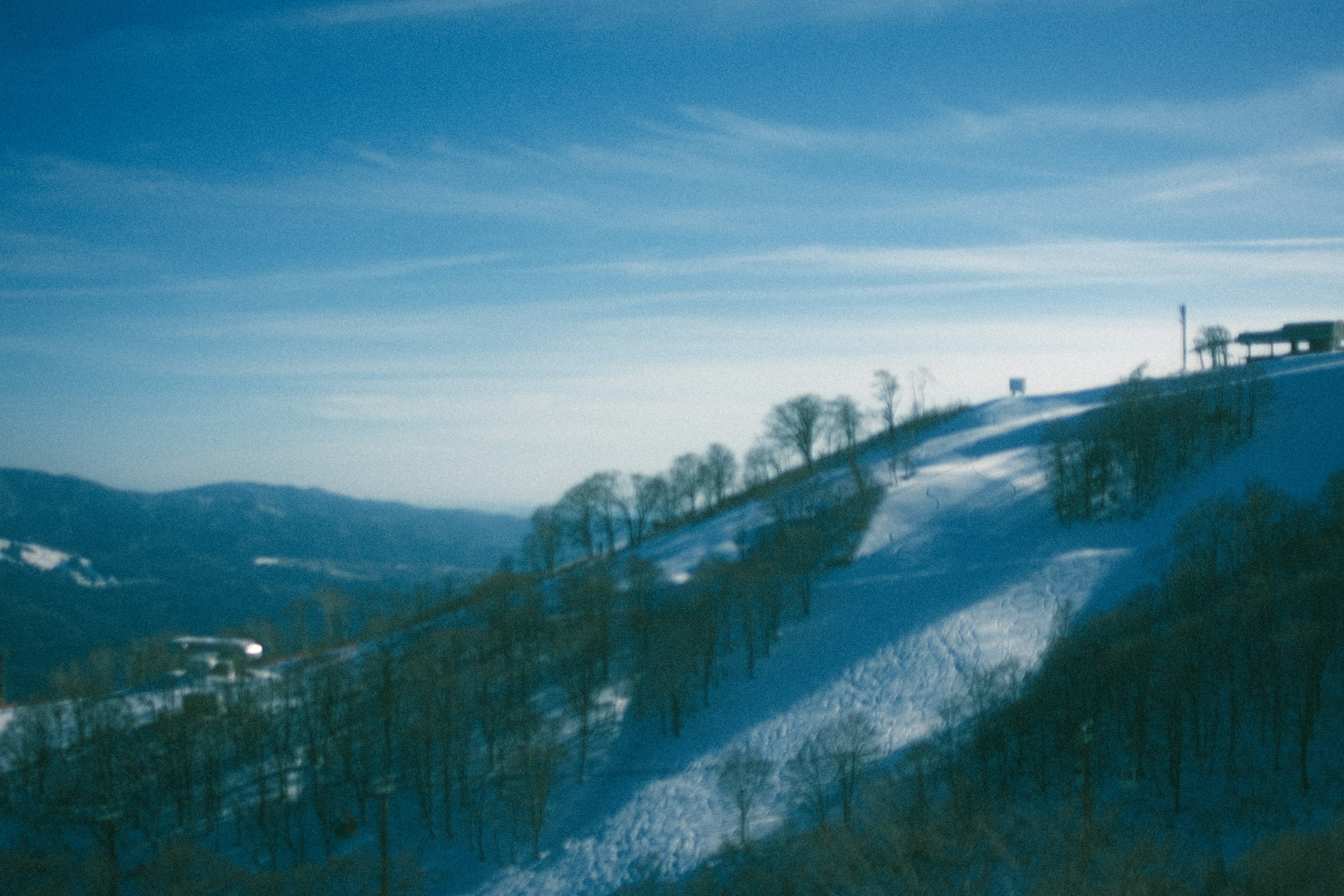 Vista escénica de colinas cubiertas de nieve bajo un cielo azul con árboles dispersos