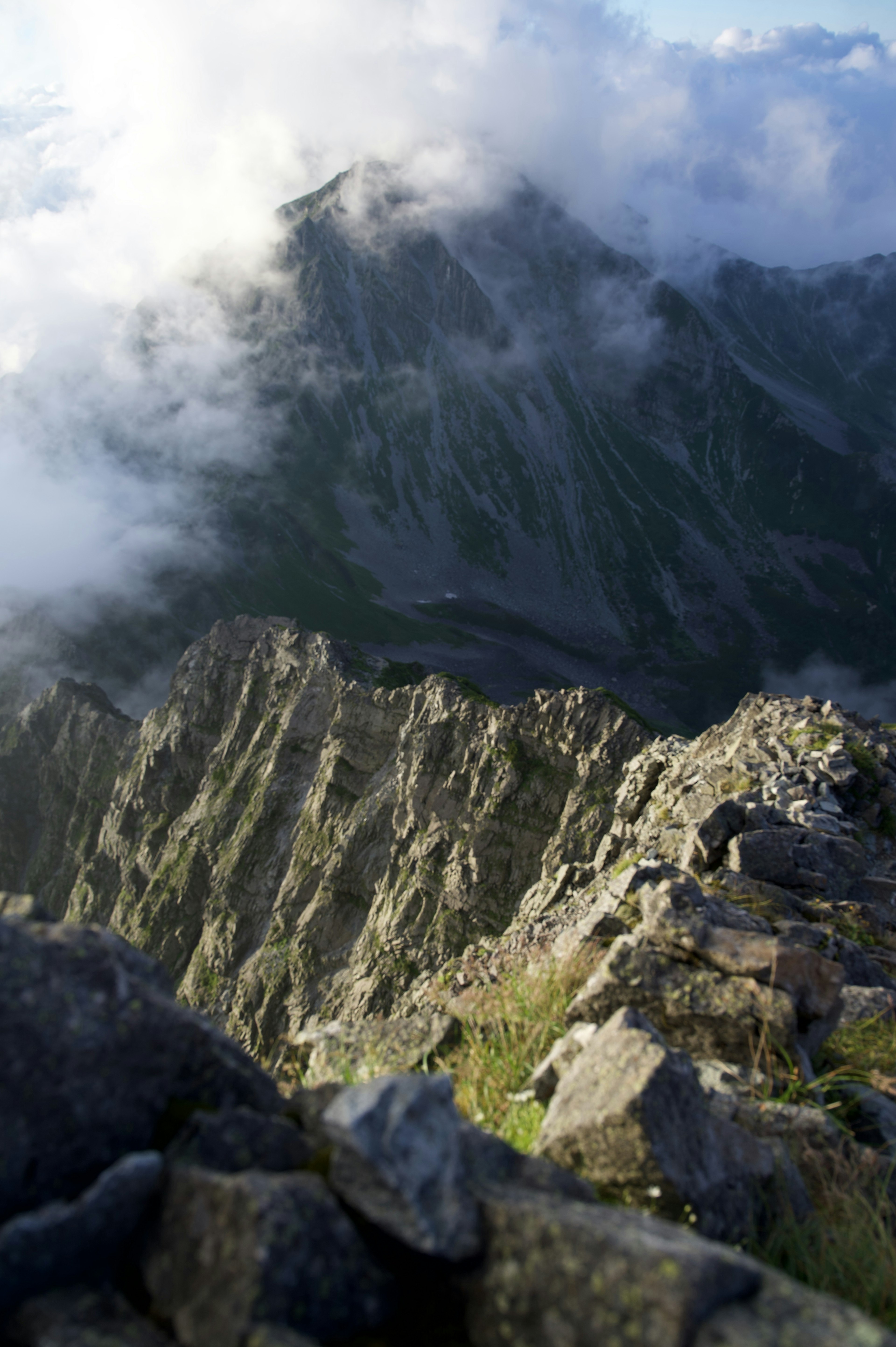 Blick vom Berggipfel bedeckt mit Wolken scharfe Gesteinsschichten und sichtbares grünes Gras