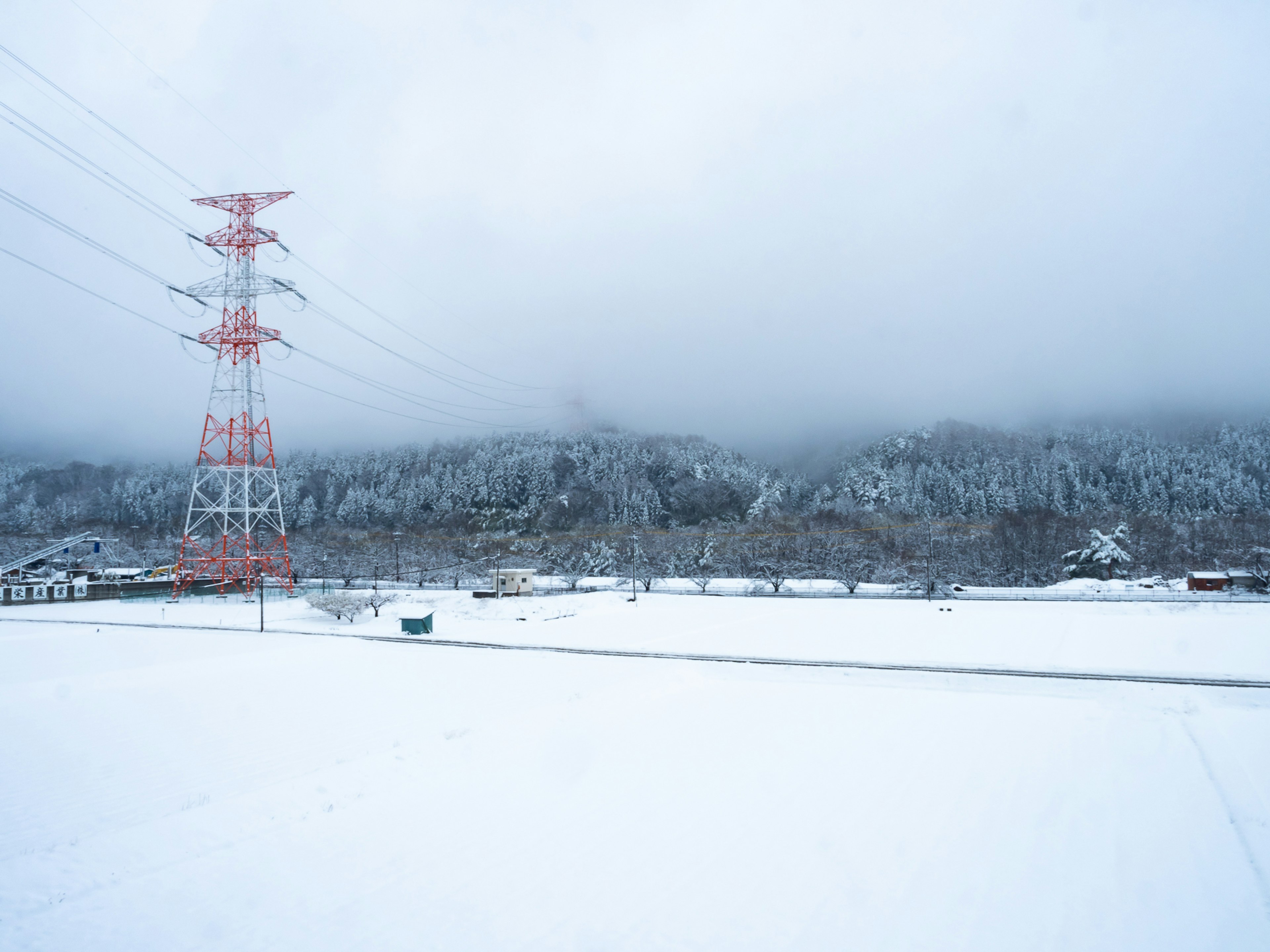 Snow-covered landscape with red power lines and mountains in the background