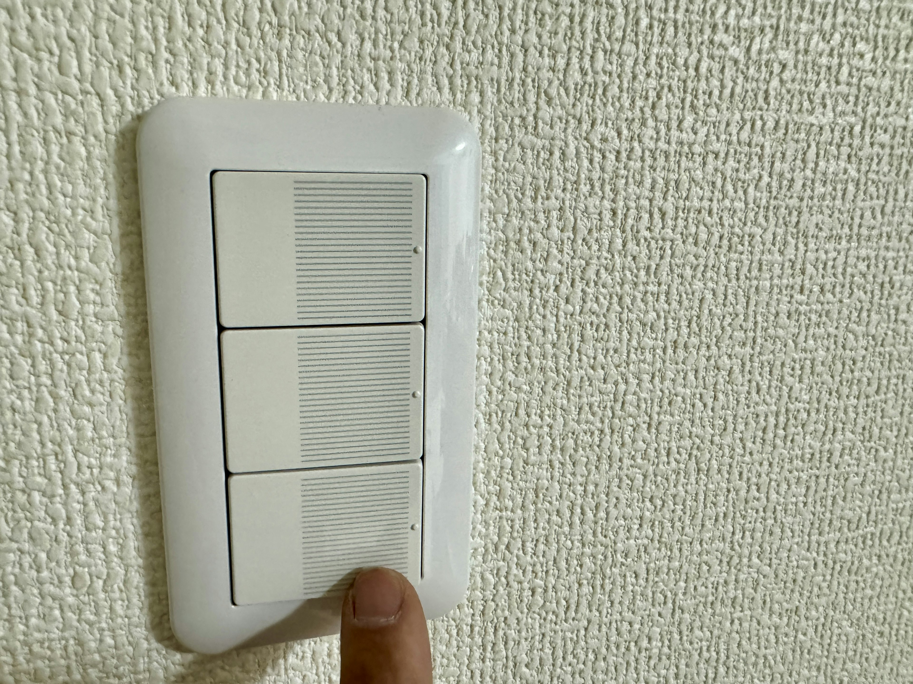 Un panel de interruptores blancos en la pared con un dedo presionándolo