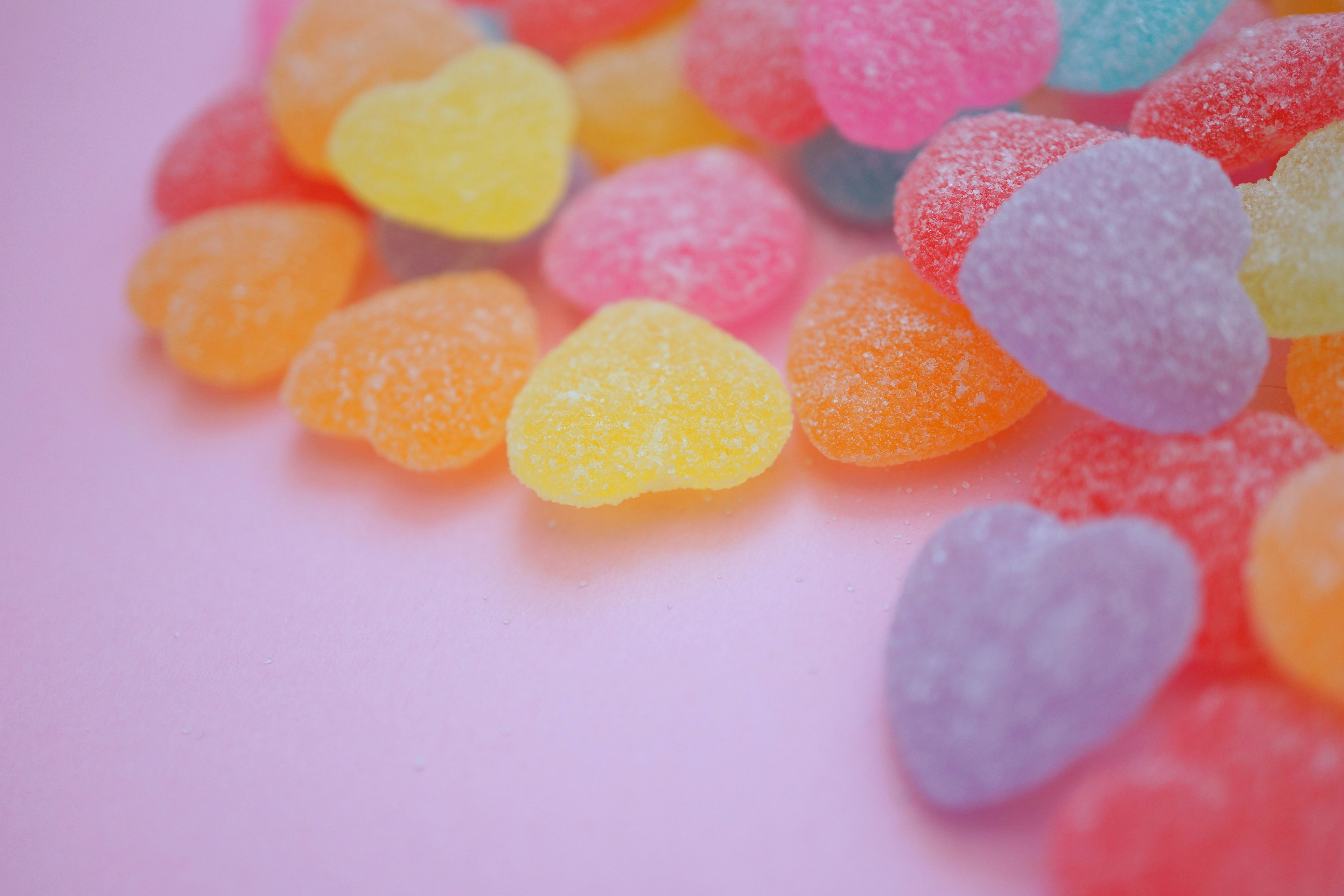 Colorful heart-shaped gummy candies scattered on a pink background