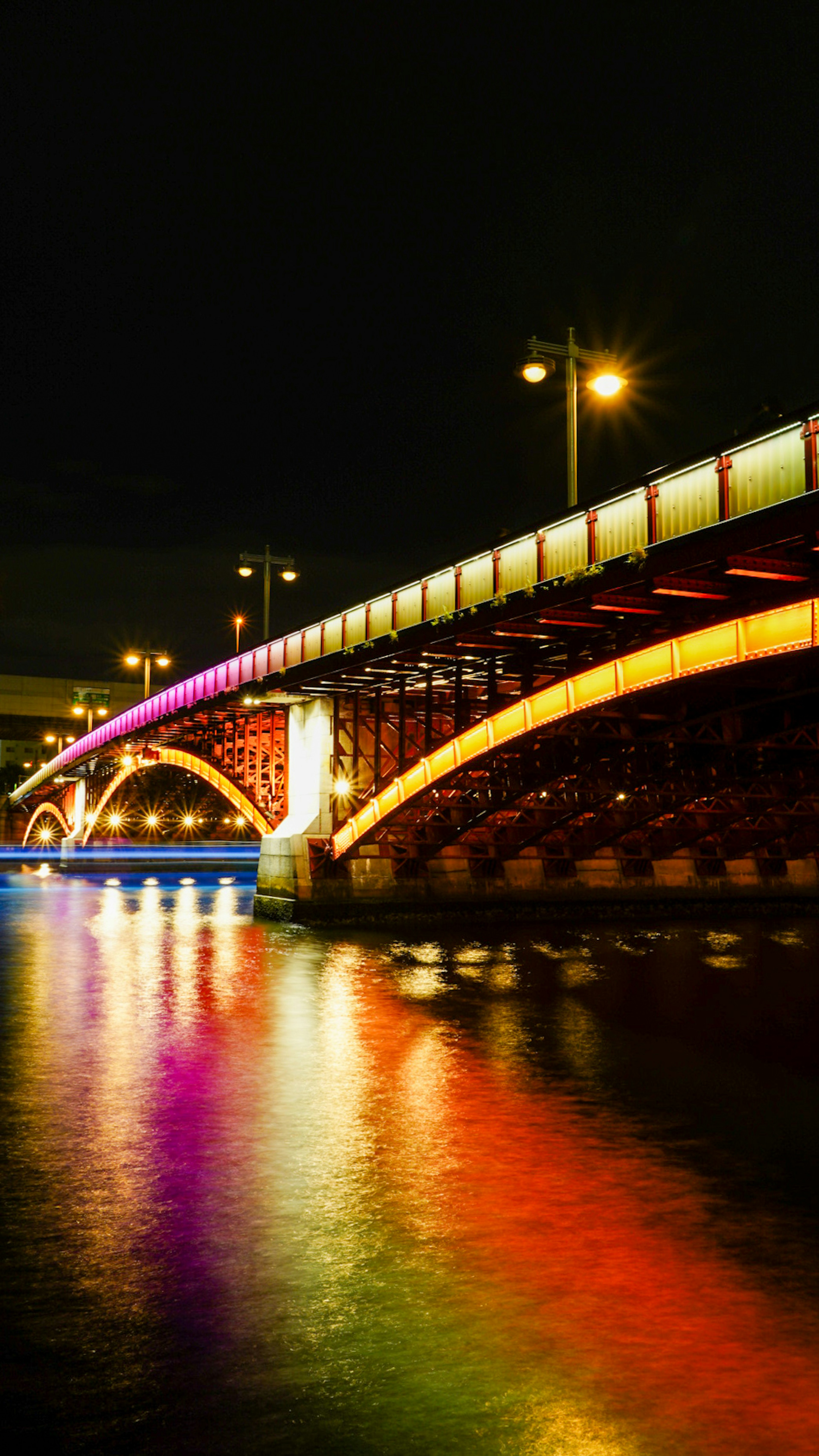 Jembatan berwarna di atas sungai di malam hari dengan refleksi