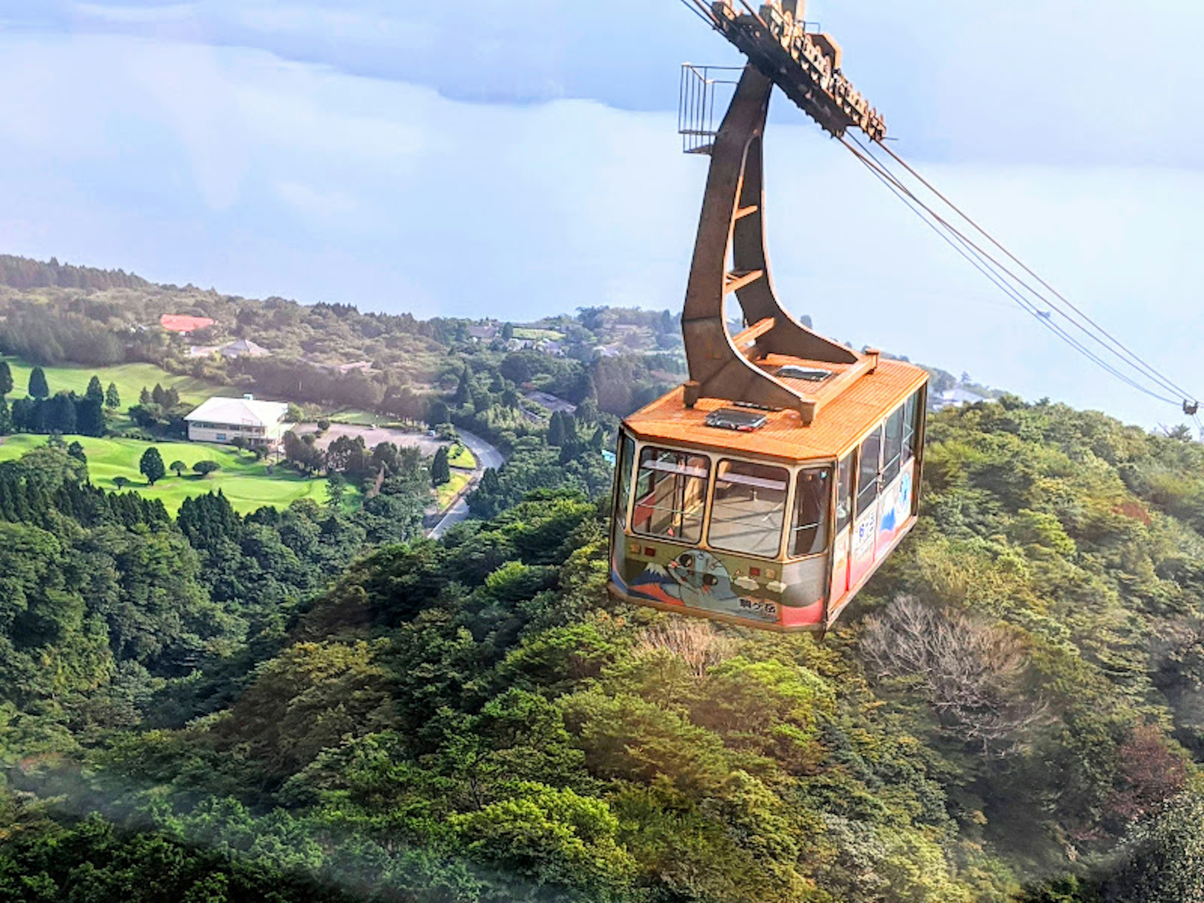 Sebuah kereta gantung di atas gunung dikelilingi oleh pepohonan hijau subur dan langit biru