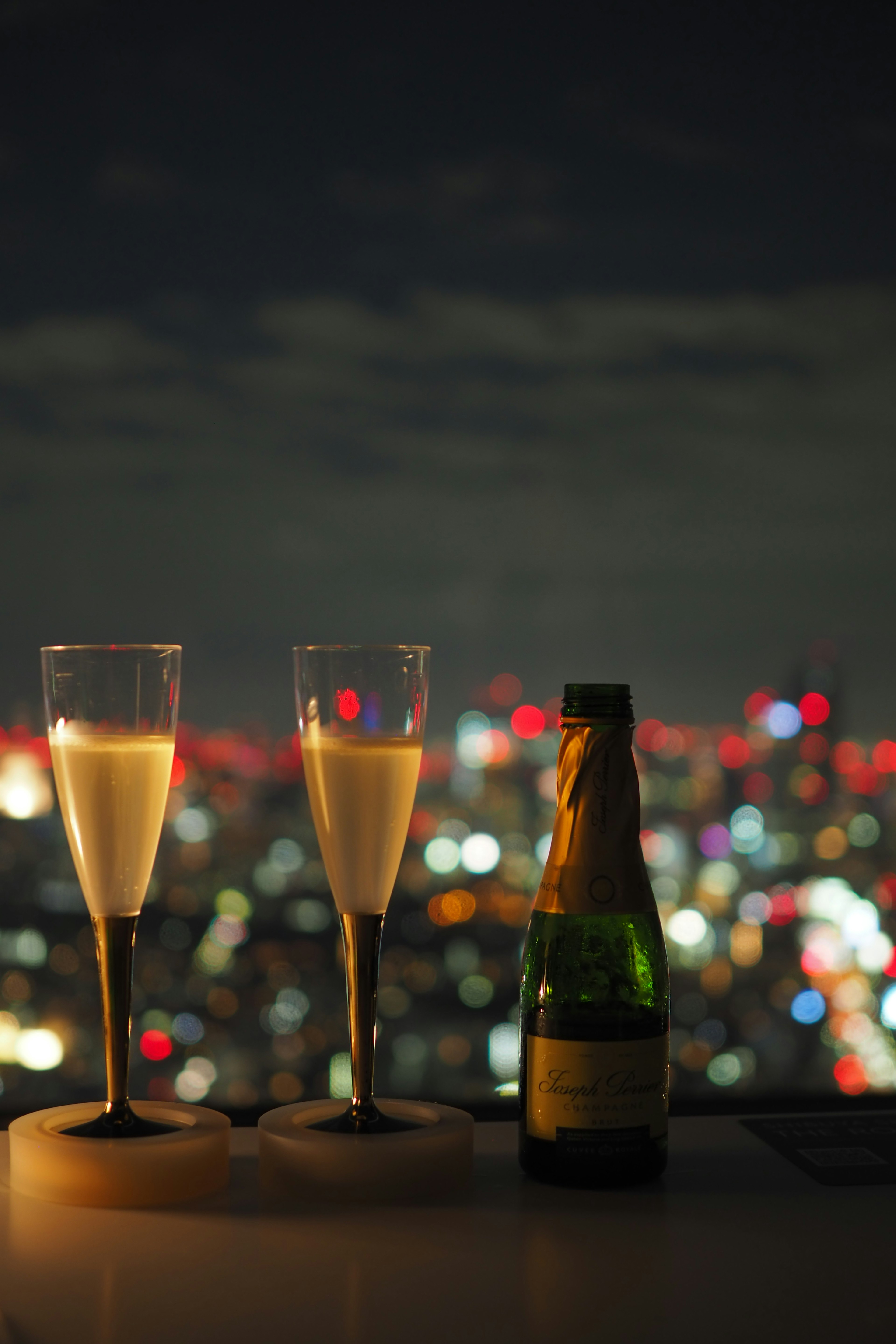 Copas de champán y botella con horizonte urbano nocturno