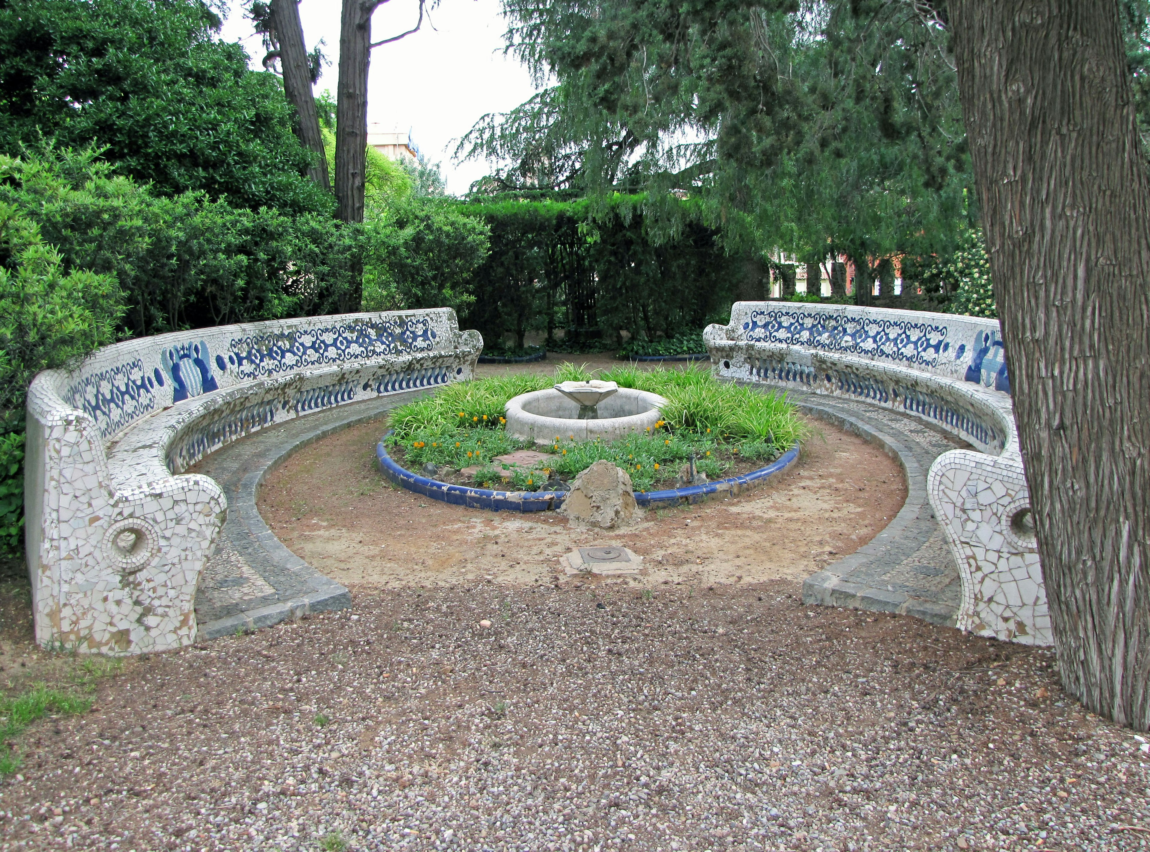 Bancs en mosaïque courbés dans un jardin vert avec une fontaine centrale