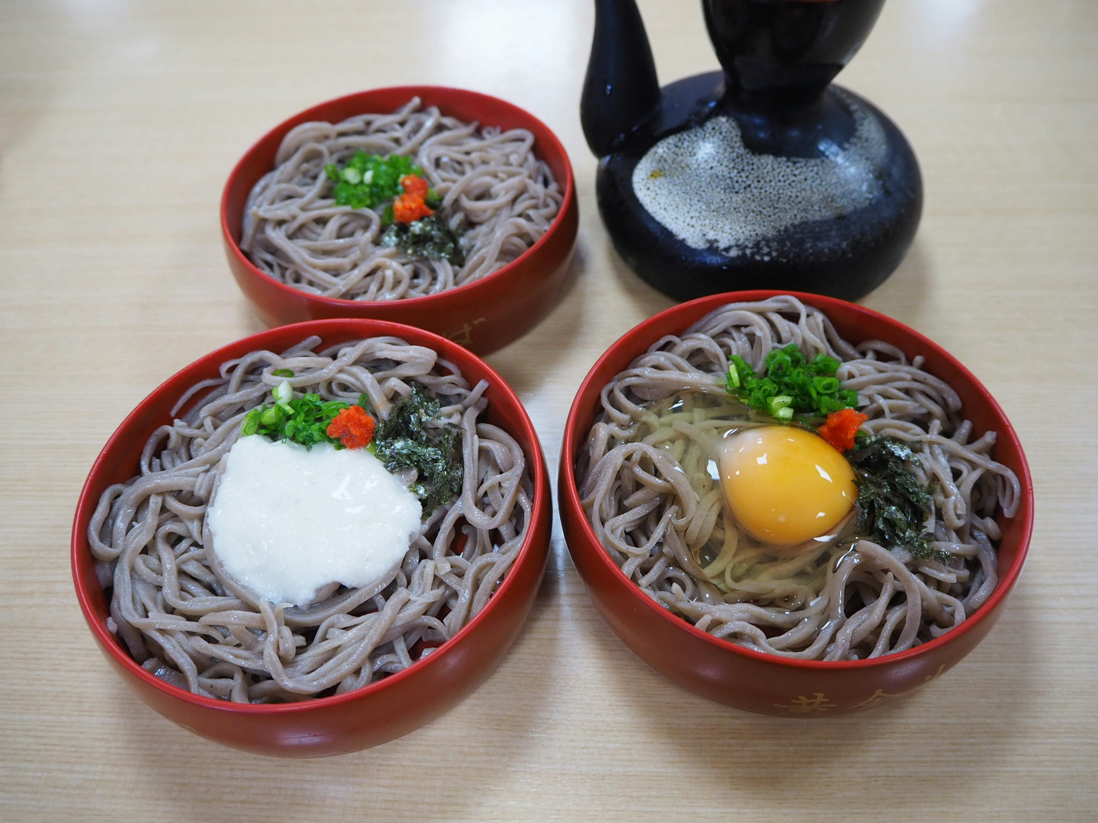 三つの赤い器に盛られたそばとトッピングの卵や野菜