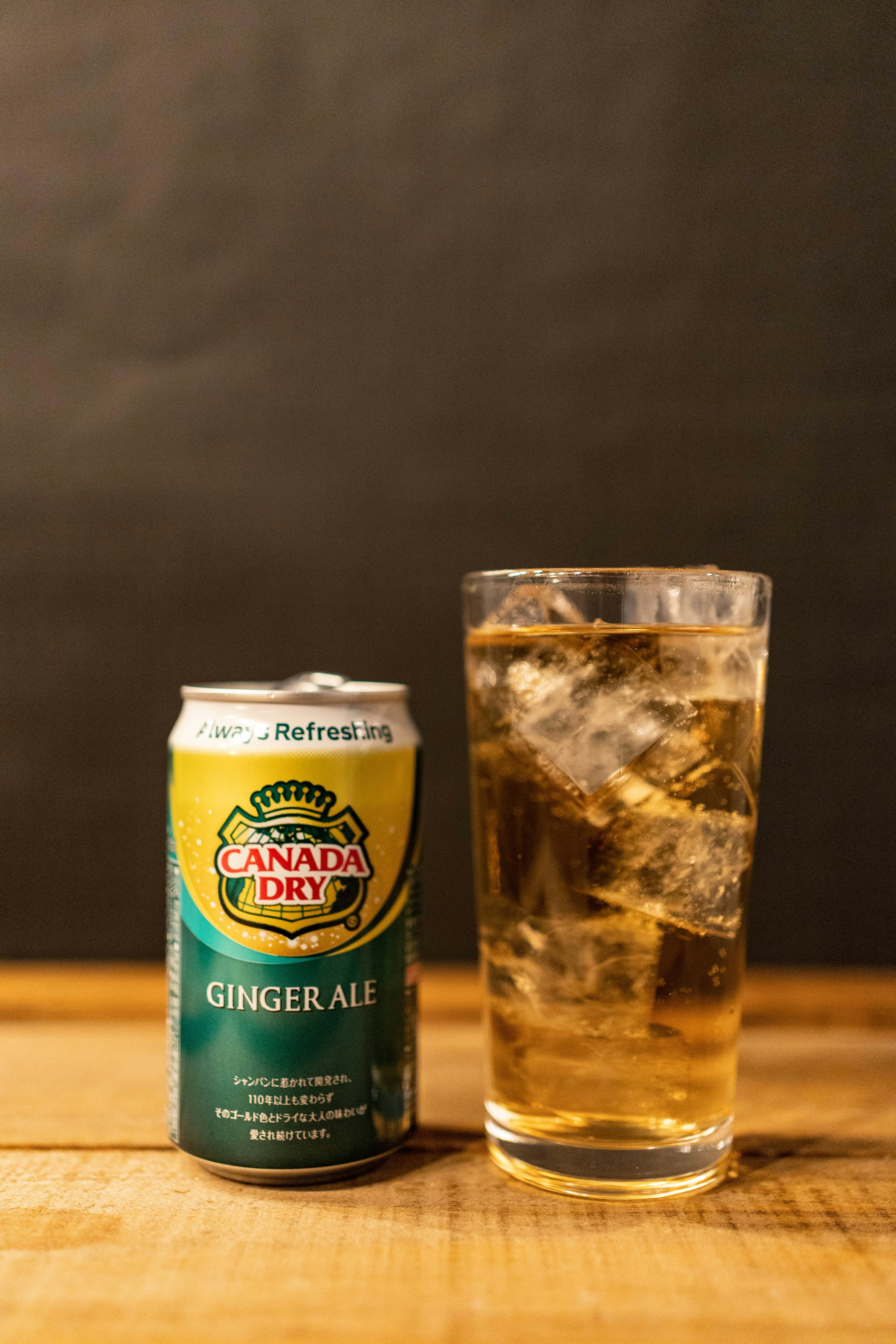 Une canette de ginger ale et un verre rempli de glace sur une table en bois