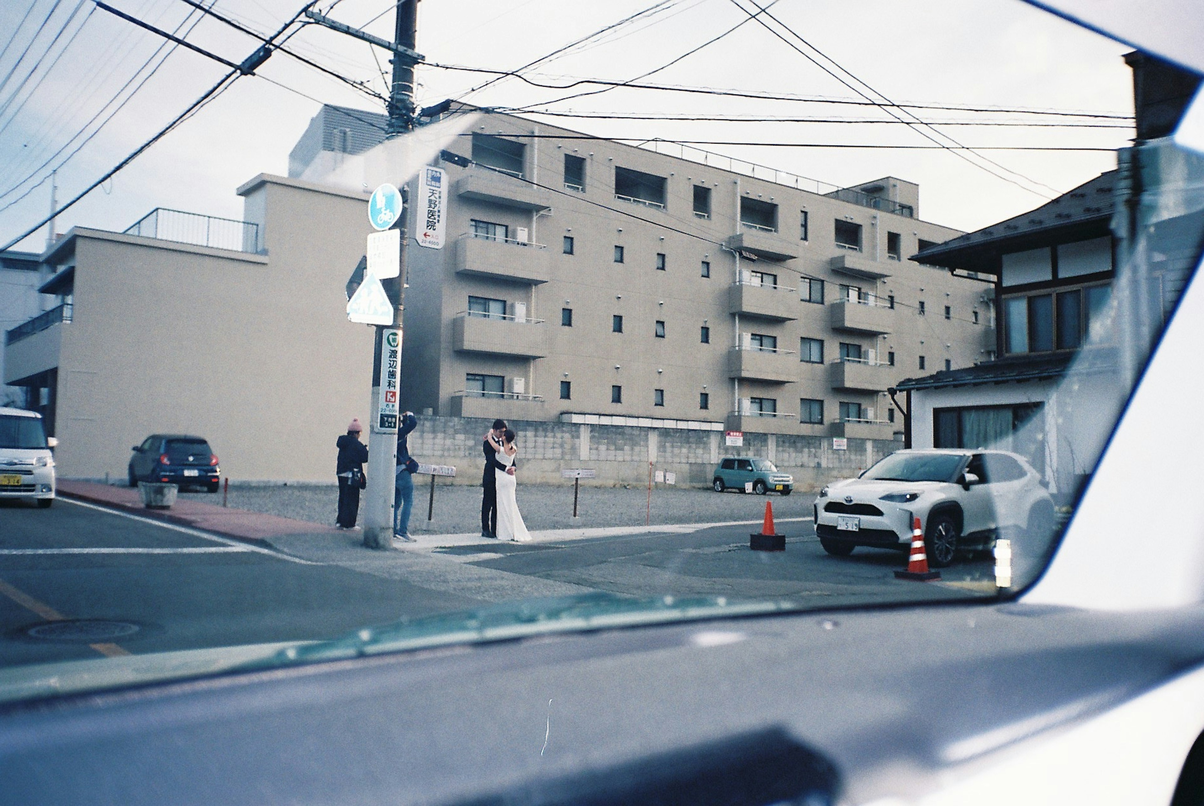 Couple in wedding attire standing on street corner with buildings in the background