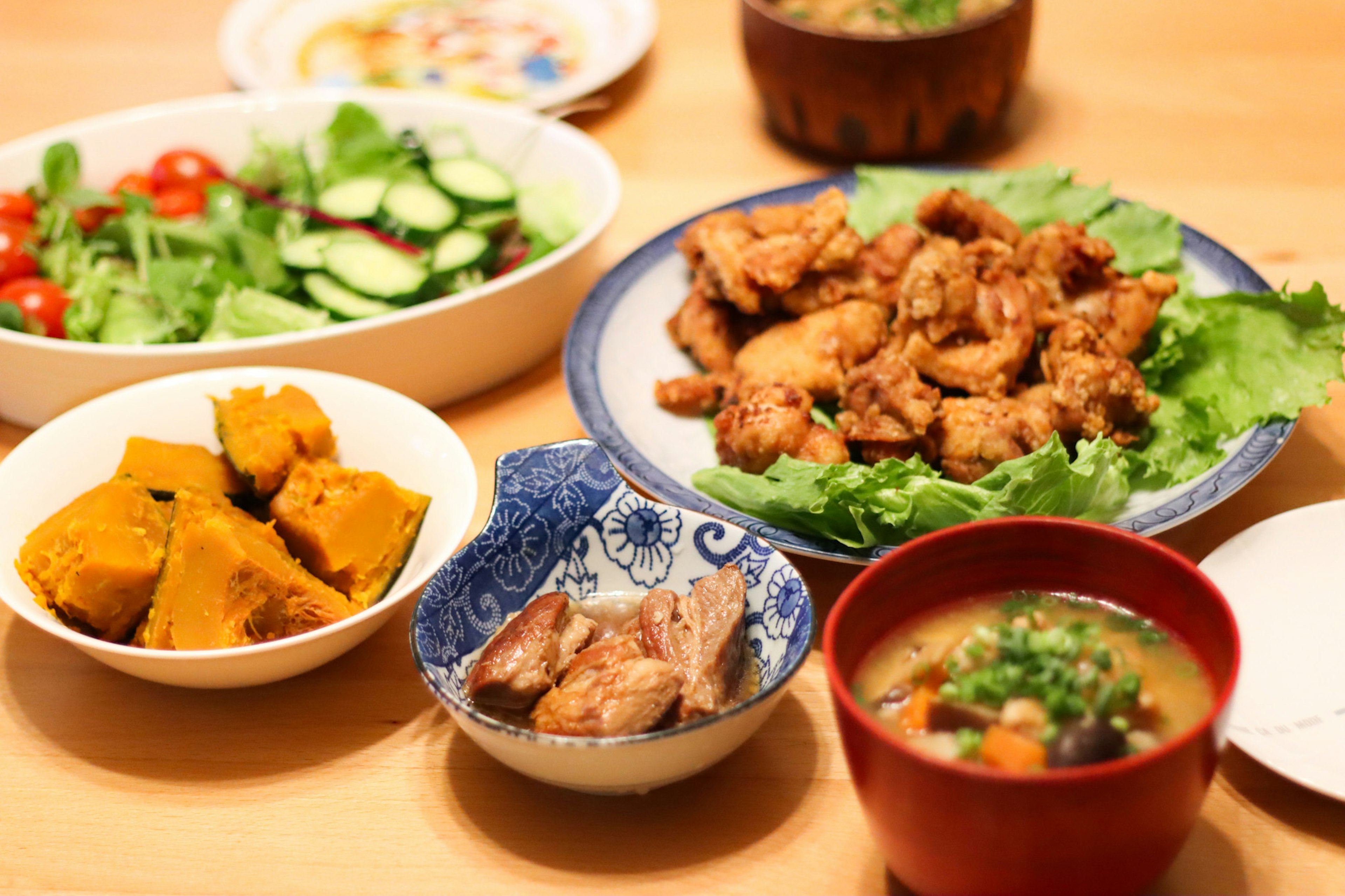 Una mesa con platos coloridos que incluyen ensalada, pollo frito, calabaza y sopa