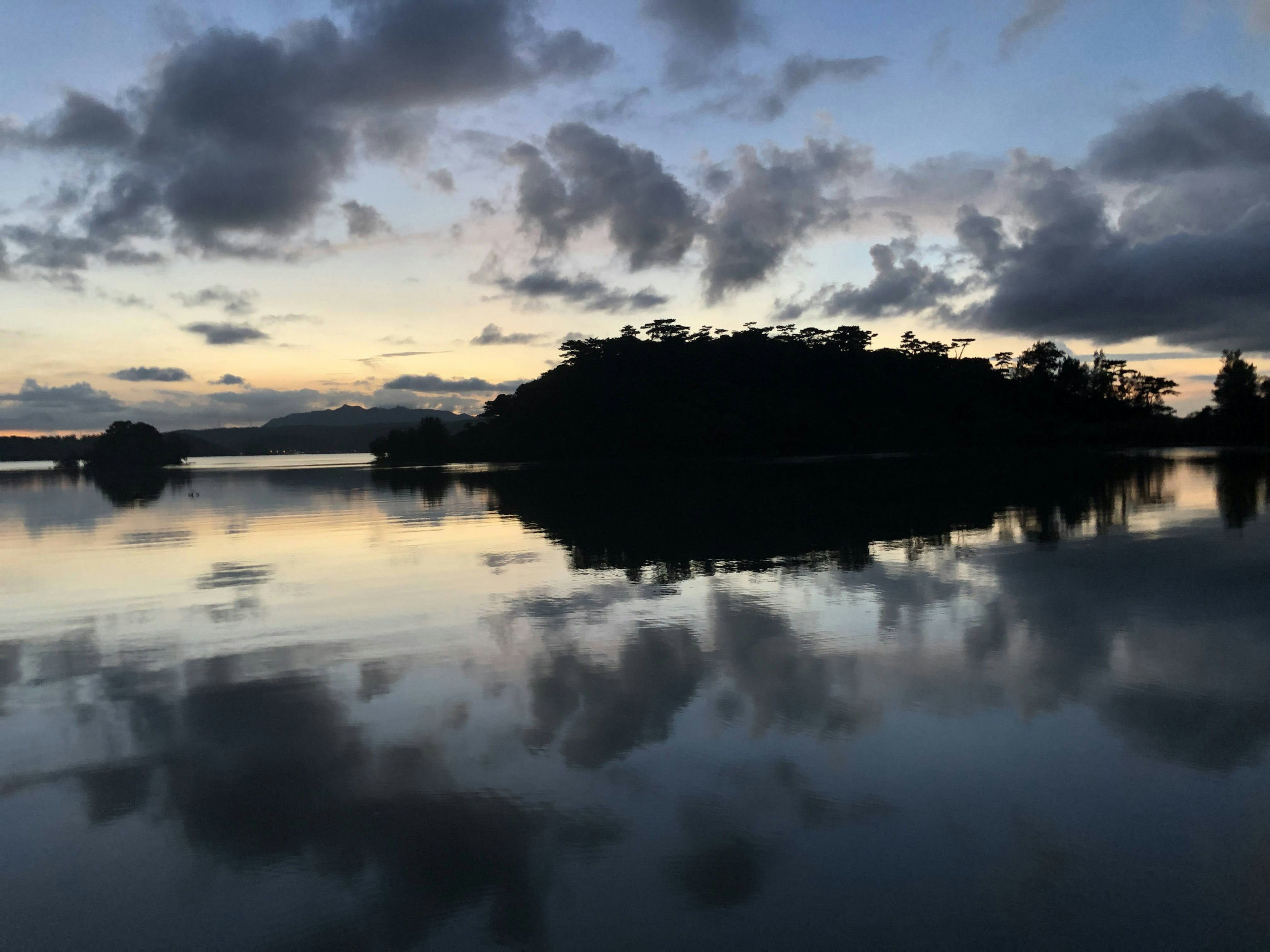 Ruhiger See, der den Sonnenuntergang und die Wolken spiegelt