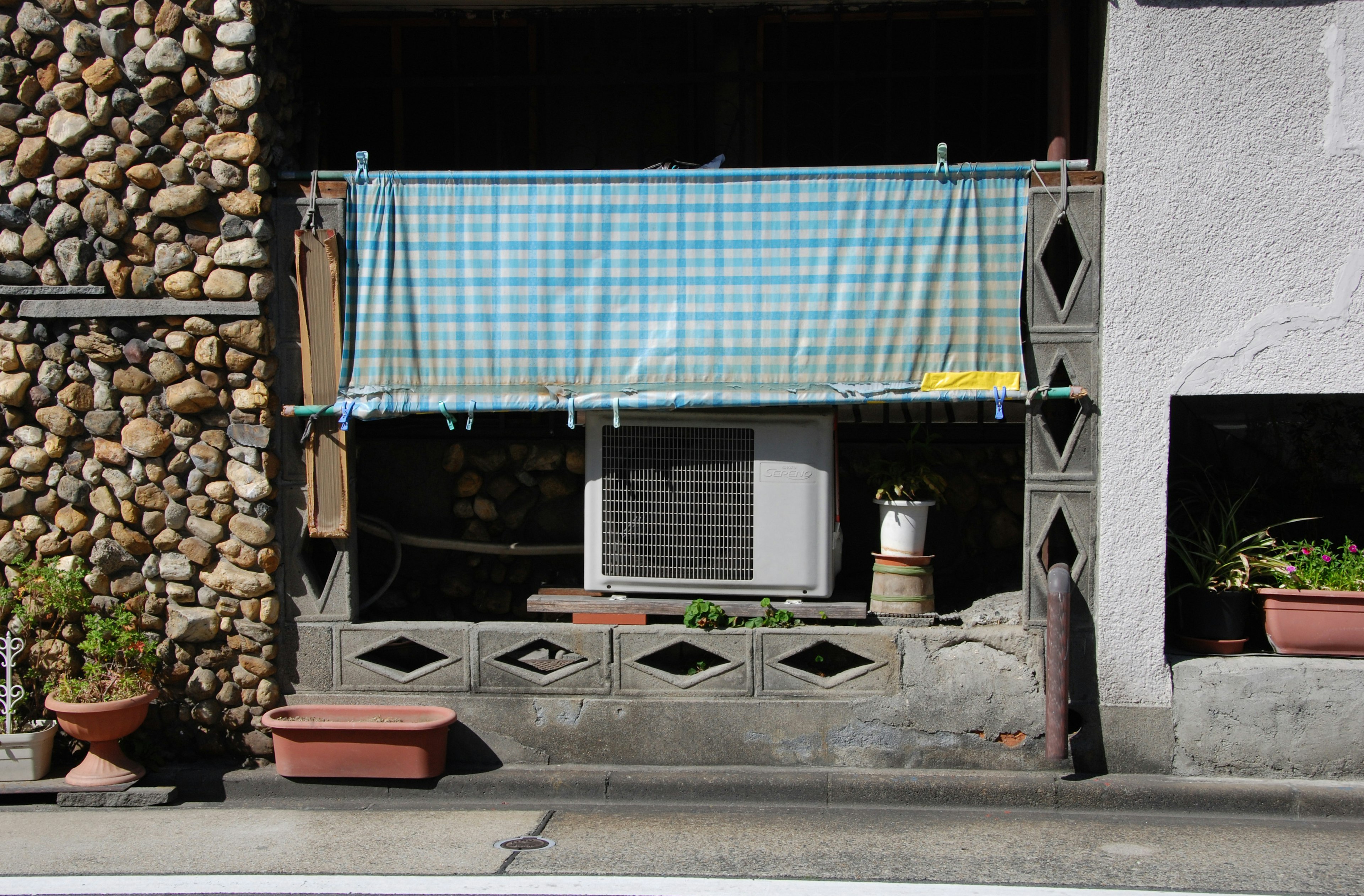 A building section with a blue checkered curtain and an air conditioner outside the window