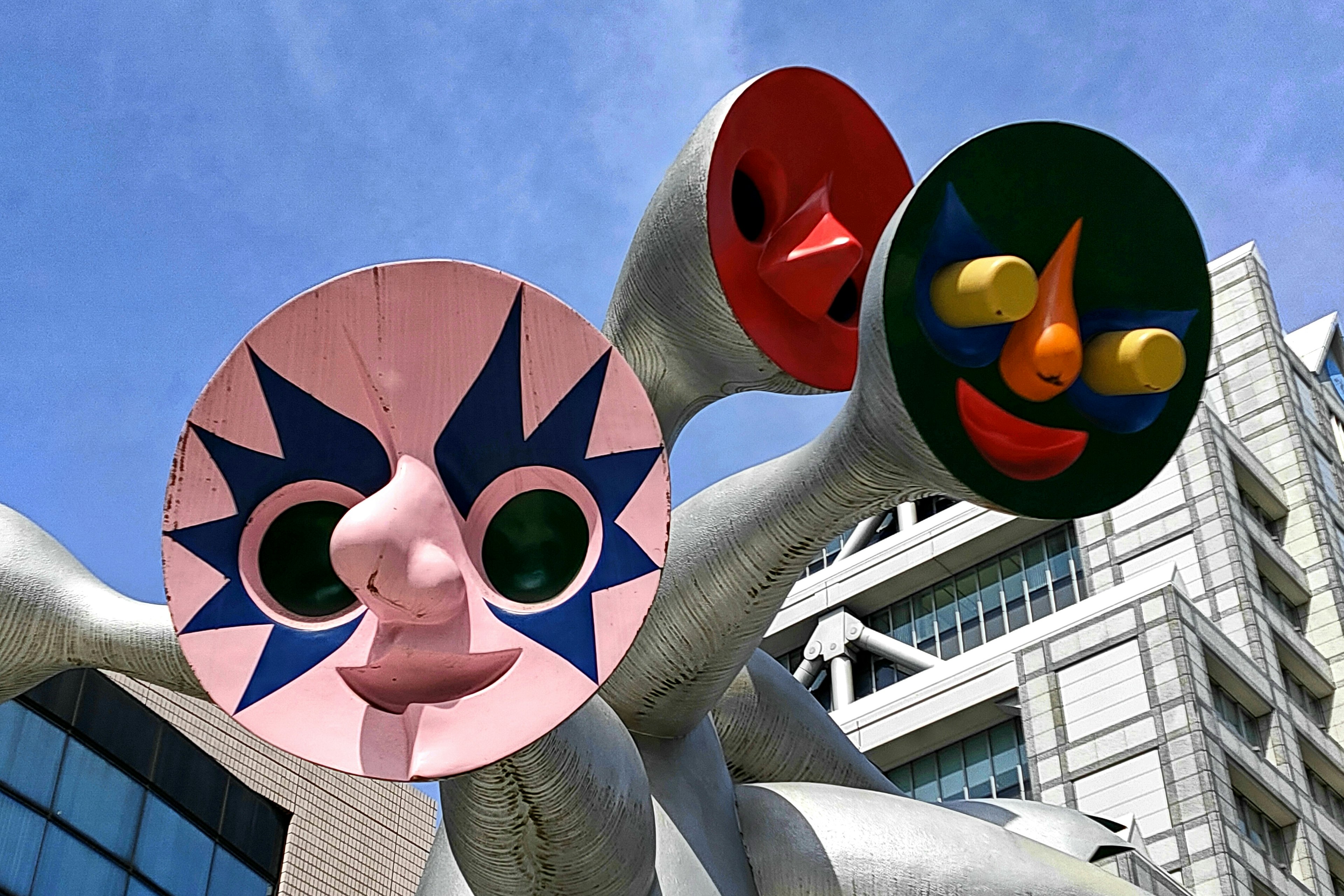 Scultura unica con volti colorati sotto un cielo blu