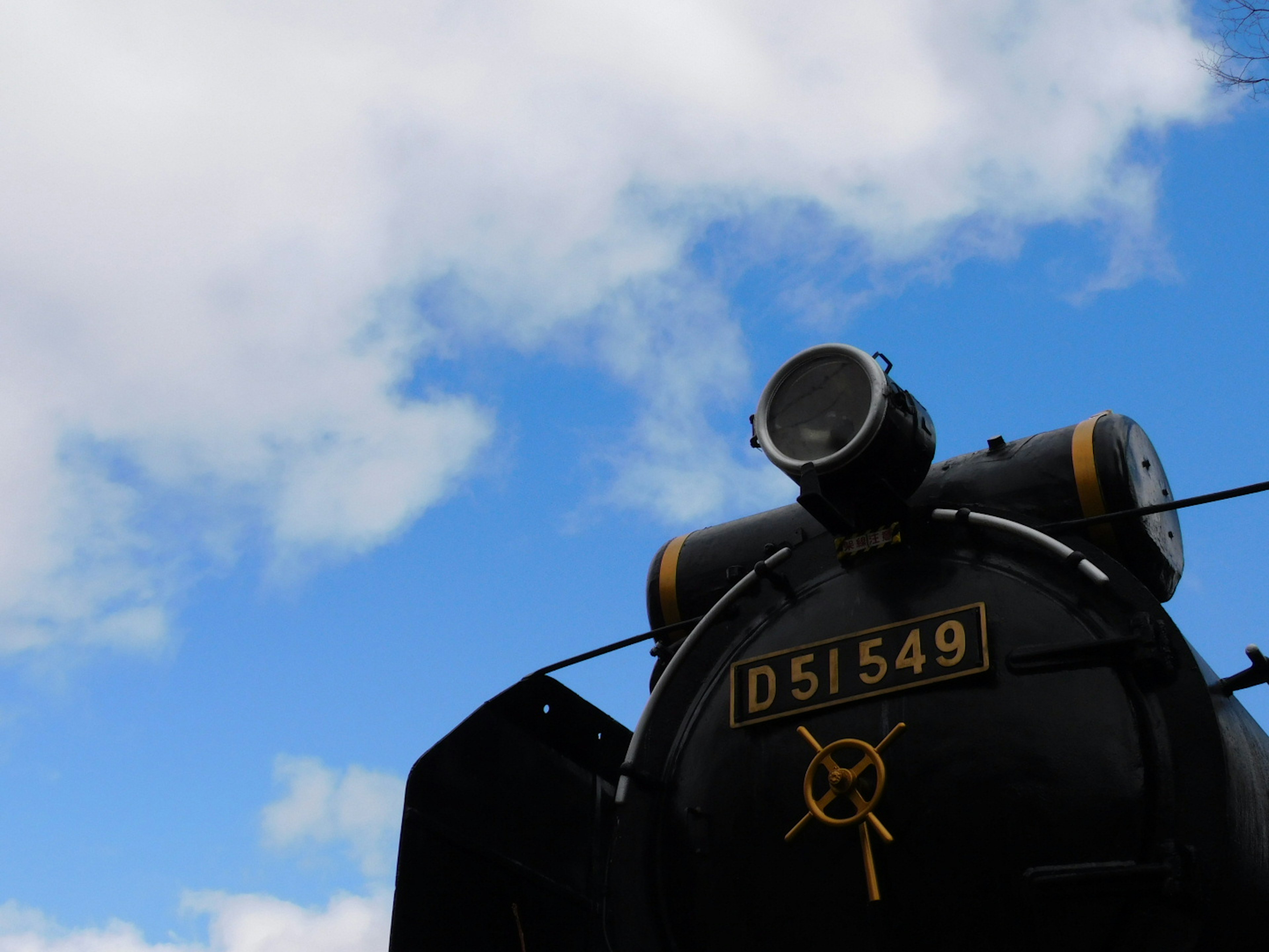 Black steam locomotive D51549 against a blue sky with clouds