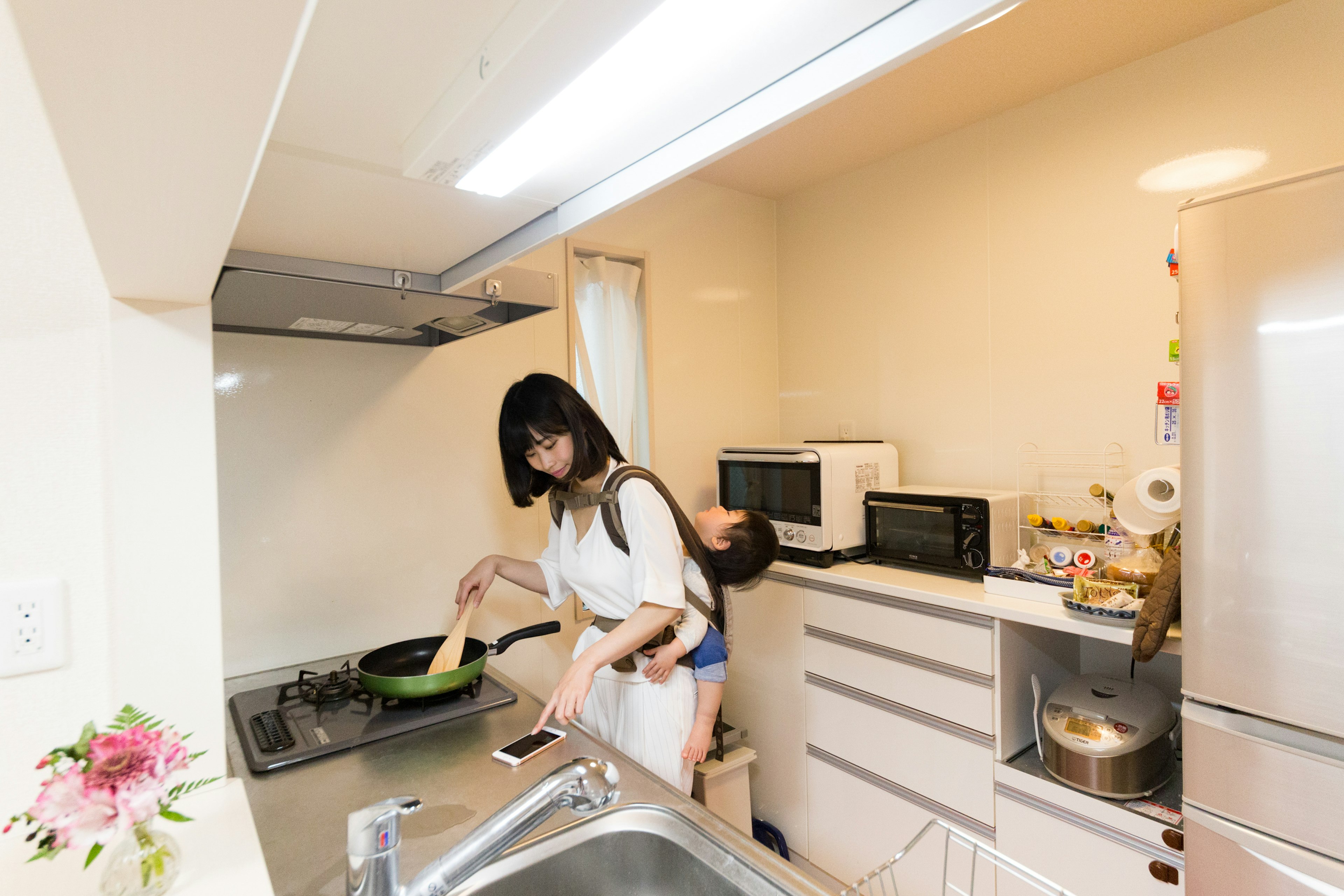 A woman cooking in a kitchen with a child on her back