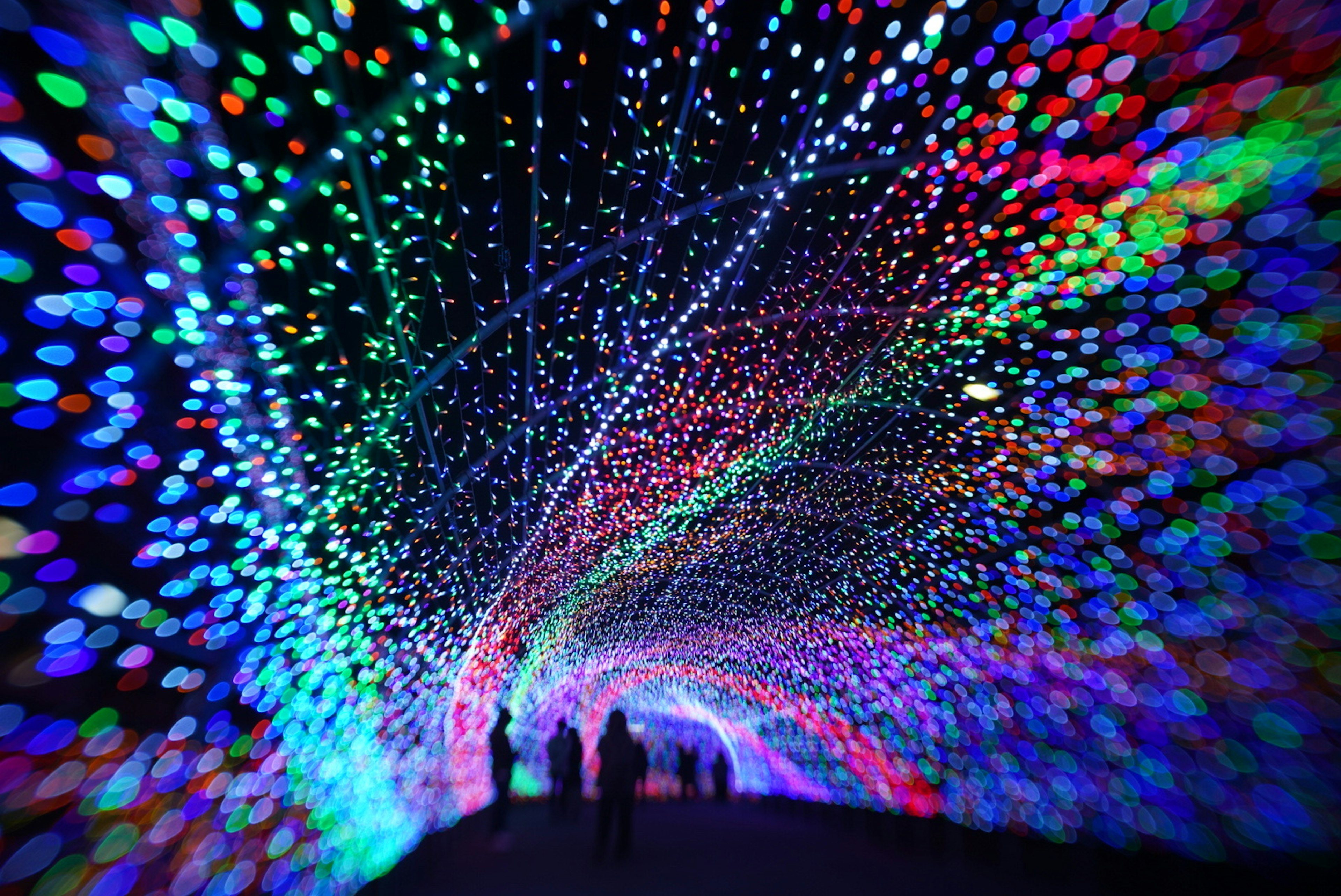 Des lumières colorées créent un effet de tunnel avec des silhouettes de personnes marchant à travers