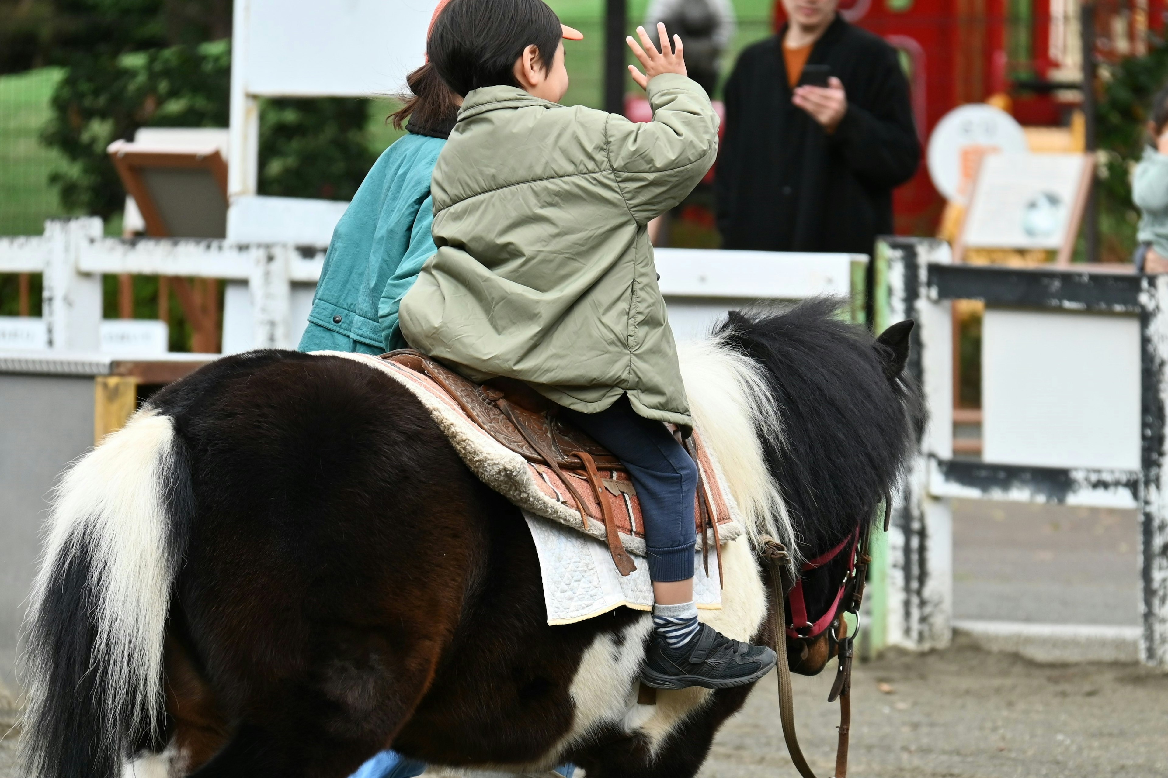 Un niño saludando mientras monta un pequeño pony