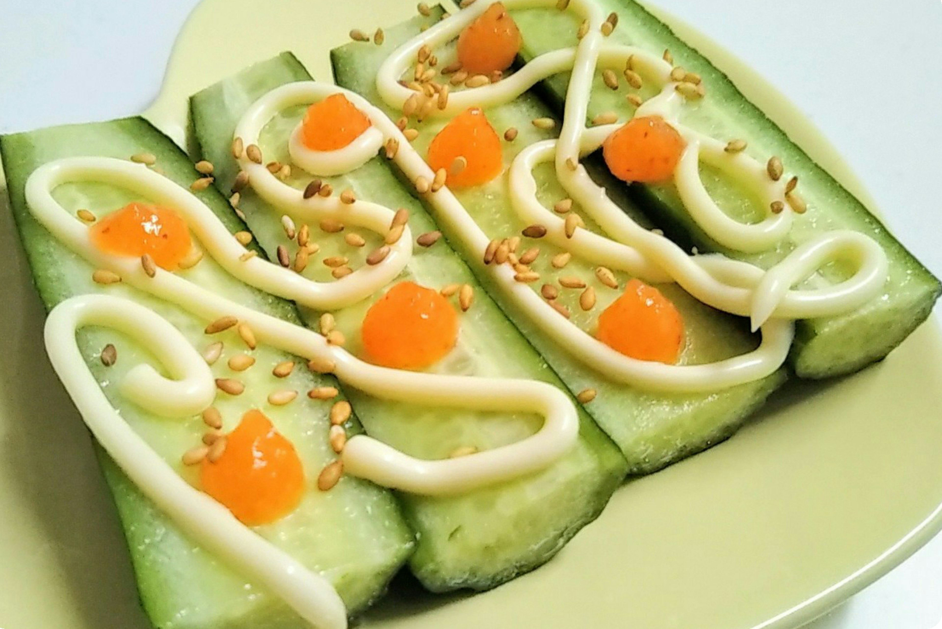 Sliced cucumbers topped with mayonnaise and orange bits on a yellow plate